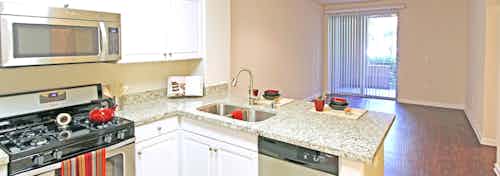 AMLI Warner Center apartment kitchen with white cabinets, stainless steel appliances and living room with hardwood floors