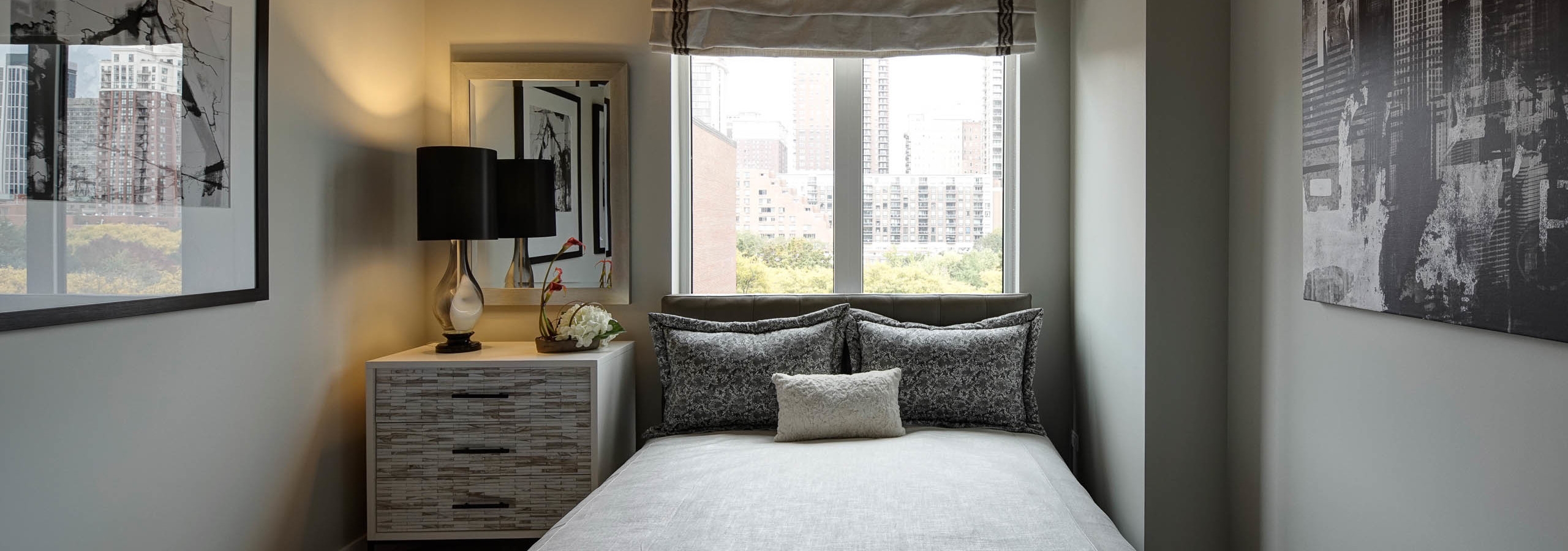 Interior view of AMLI Lofts bedroom with grey and white furnishings and sunlight coming in from a window on the middle wall