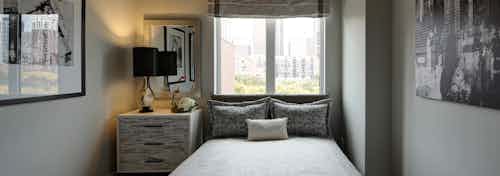 Interior view of AMLI Lofts bedroom with grey and white furnishings and sunlight coming in from a window on the middle wall