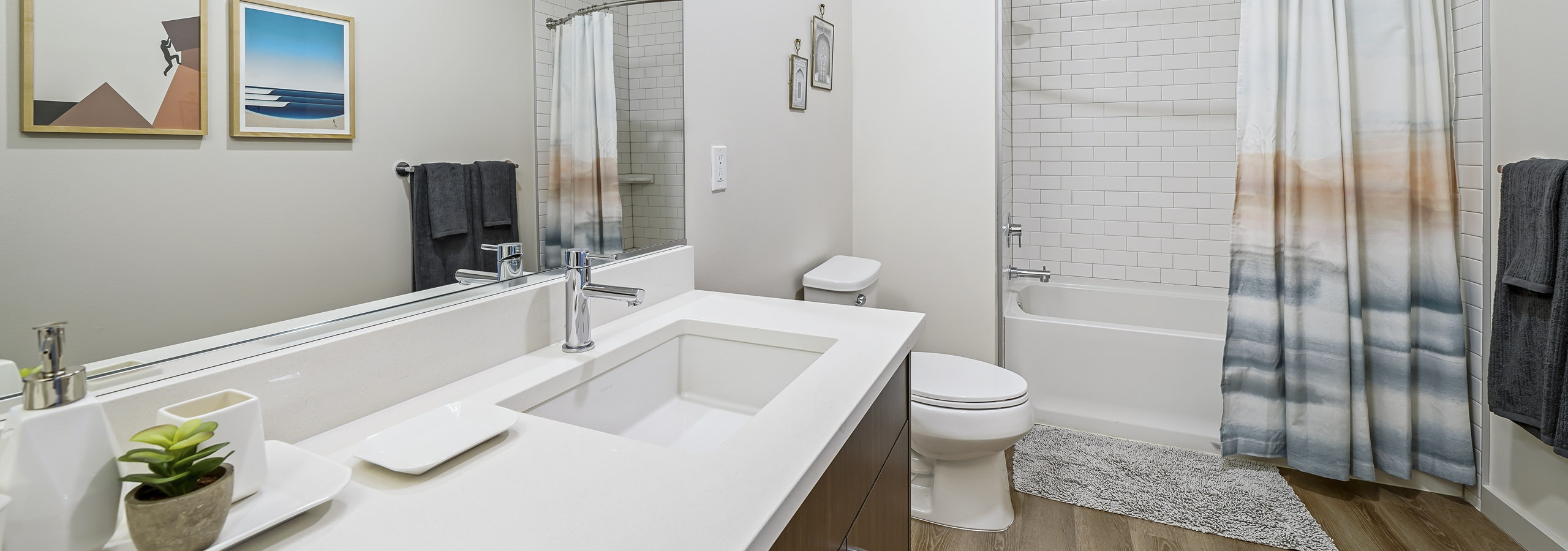Double bathroom vanity with brown cabinets and large mirror and white quartz countertops at AMLI Spring District apartments