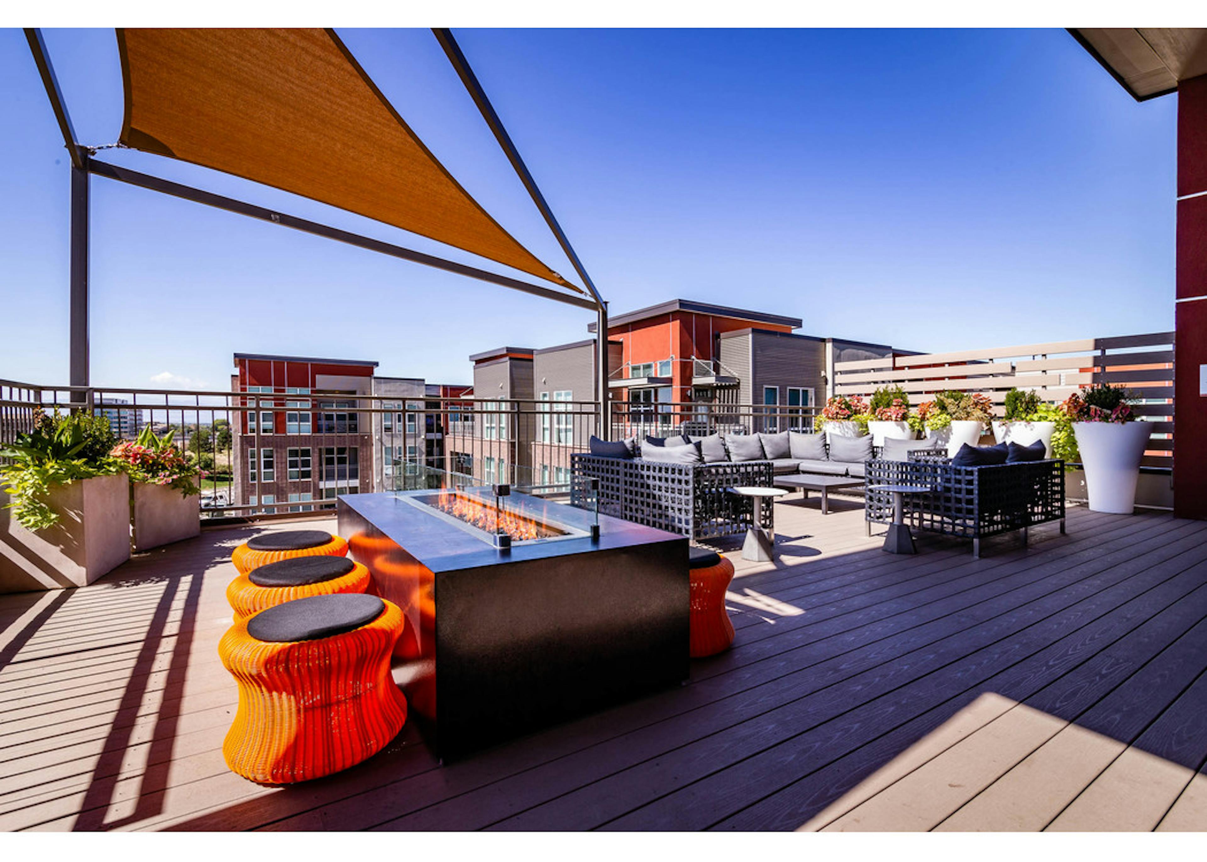 View of the rooftop at AMLI Dry Creek apartments with a fire pit and surrounding short stools as well as a sectional couch 