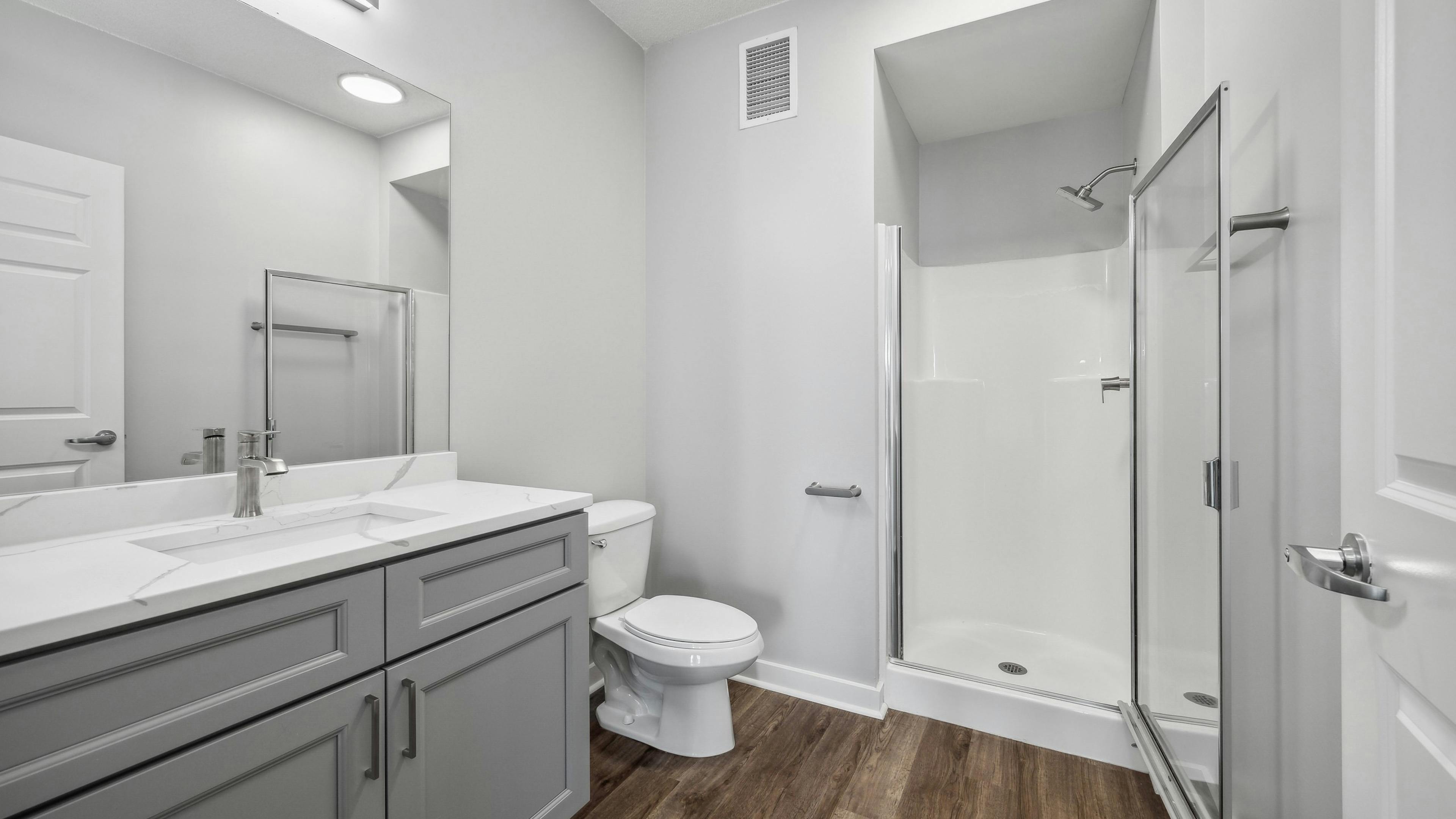 AMLI 900 bathroom featuring a gray vanity with white quartz counter and mirror above and a white toilet and stand up shower