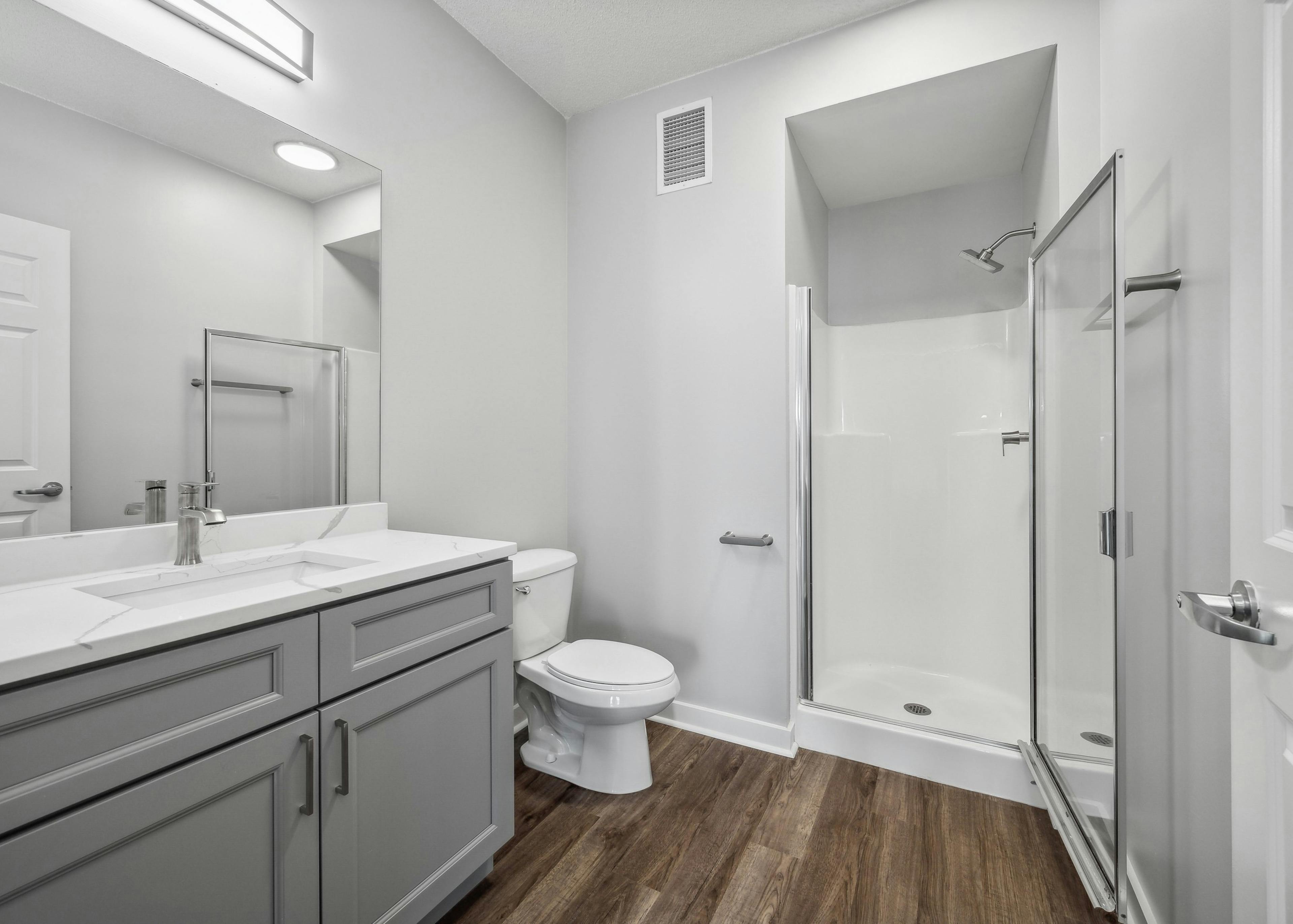 AMLI 900 bathroom featuring a gray vanity with white quartz counter and mirror above and a white toilet and stand up shower