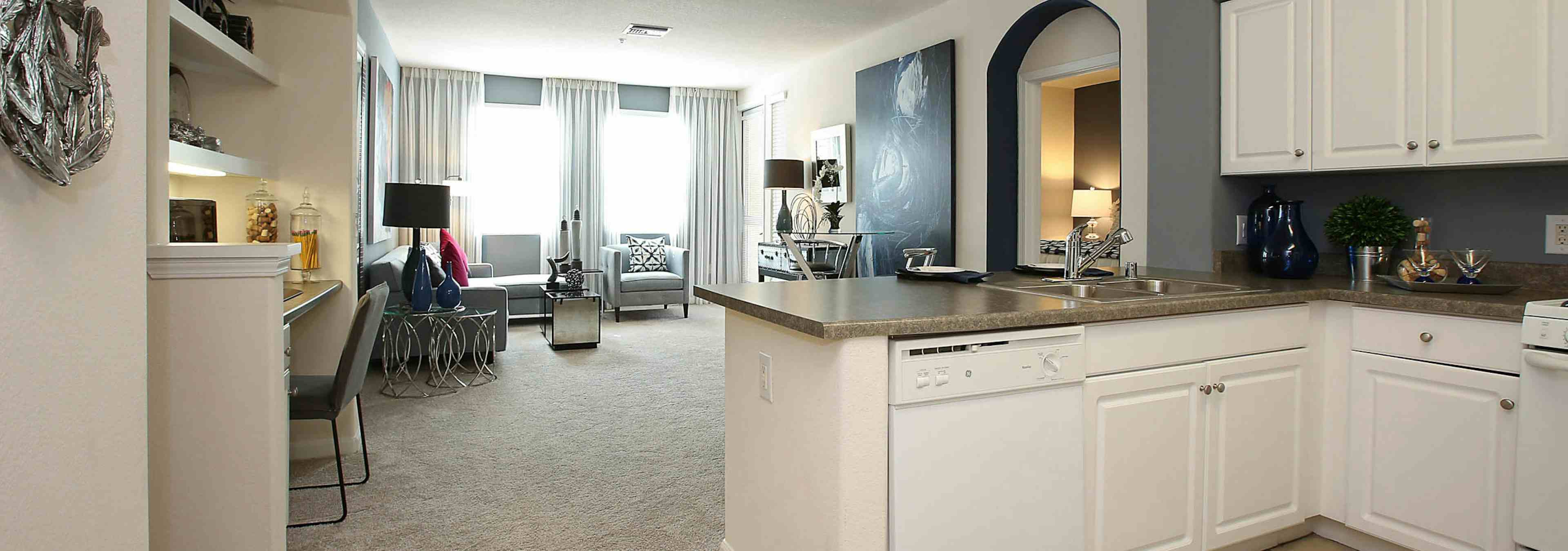 Interior view of AMLI Warner Center apartment kitchen and furnished living room with carpet, built-in desk and large windows