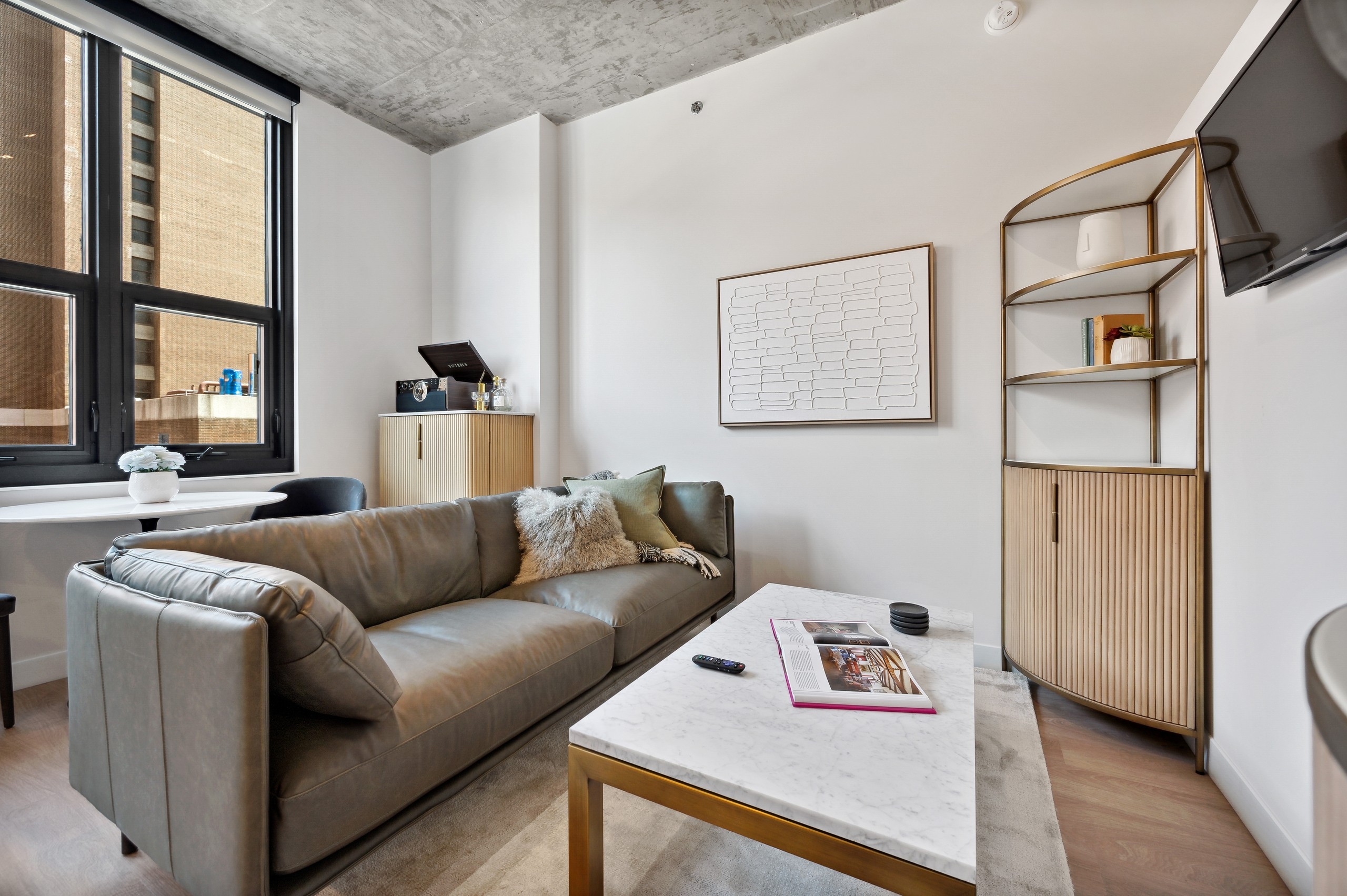 AMLI 808 living room with large window and grey couch with white marble coffee table and corner shelf with white artwork