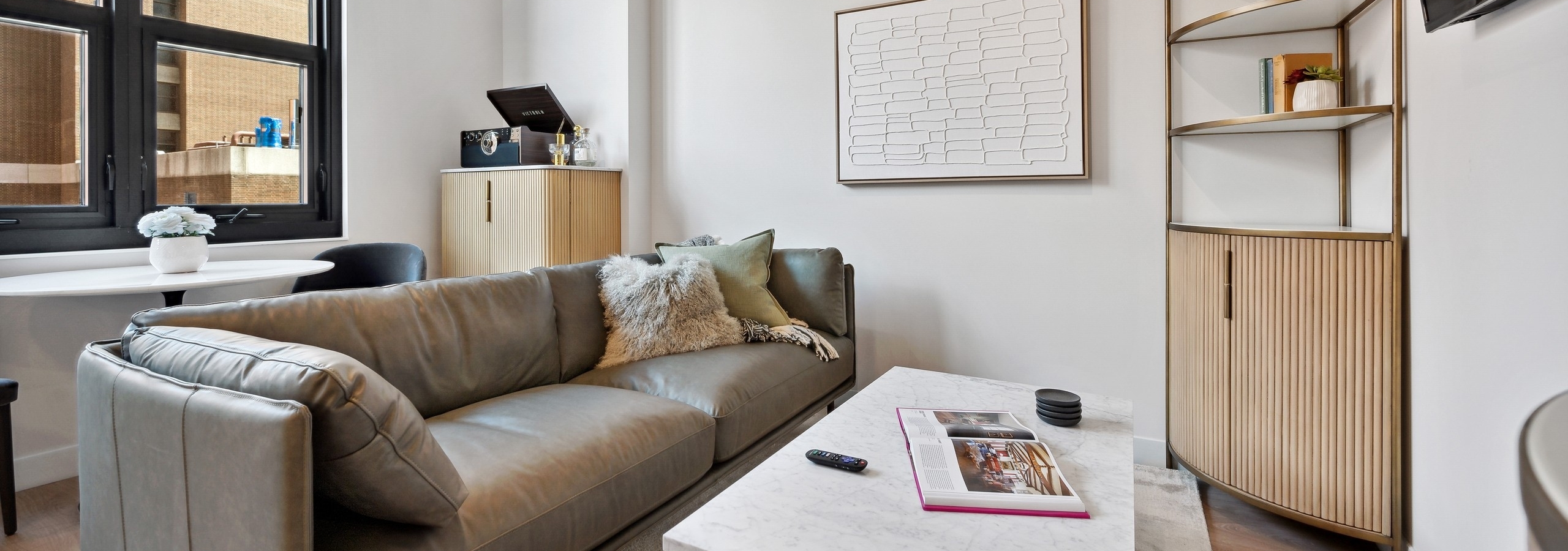 AMLI 808 living room with large window and grey couch with white marble coffee table and corner shelf with white artwork