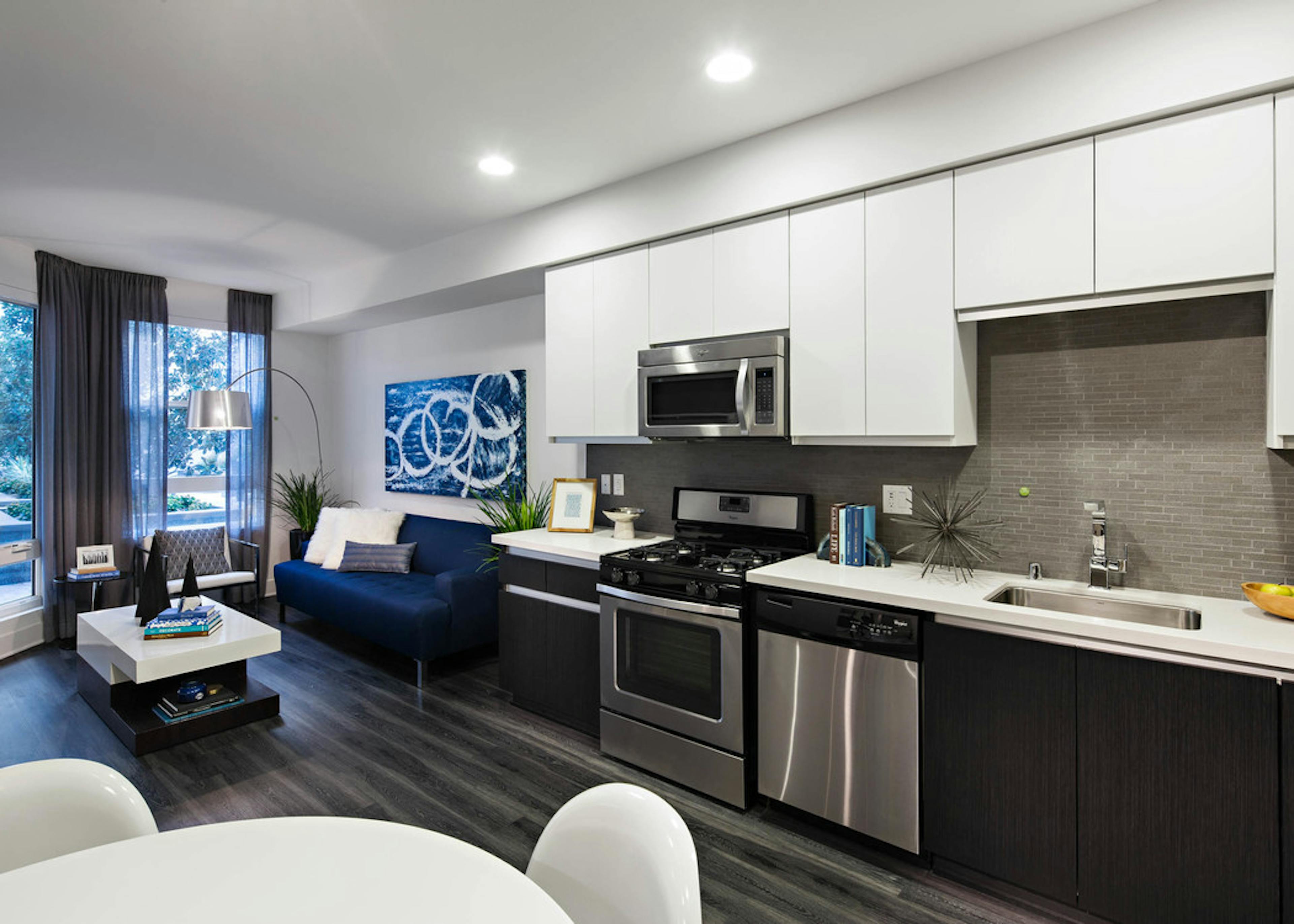 Interior of AMLI Lex on Orange apartment kitchen with white cabinetry and living room with blue couch and hard wood floors 