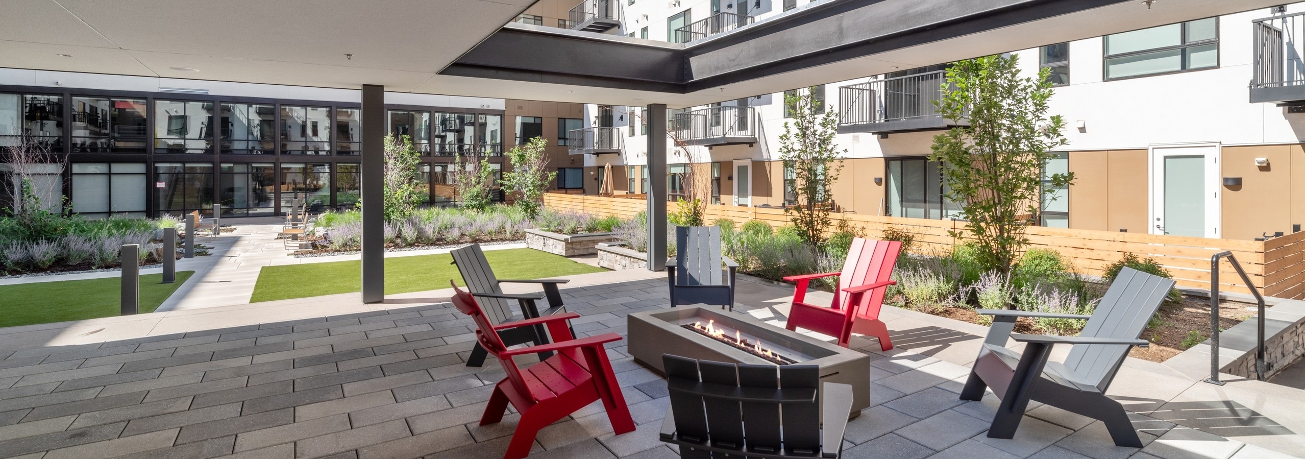 Courtyard garden at AMLI Broadway Park with Adirondack chairs around rectangular fire pit under roof with large opening