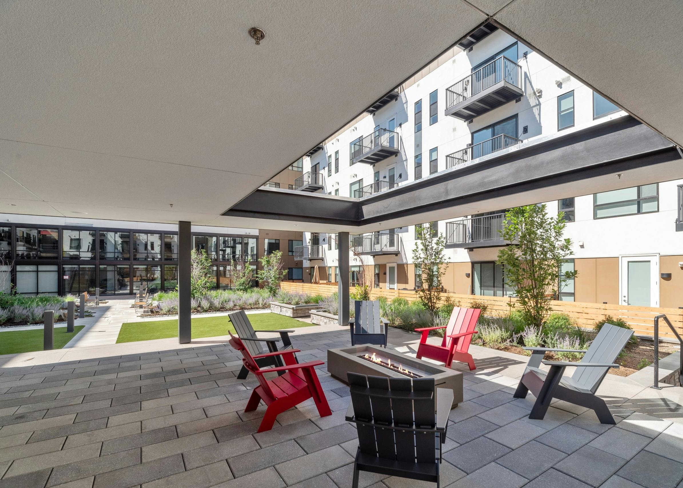 Courtyard garden at AMLI Broadway Park with Adirondack chairs around rectangular fire pit under roof with large opening