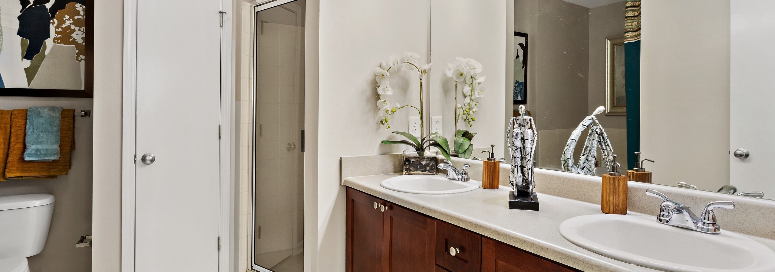 Bathroom with dark wood vanity with two sinks and large mirror above and walk in shower at AMLI Lindbergh apartments