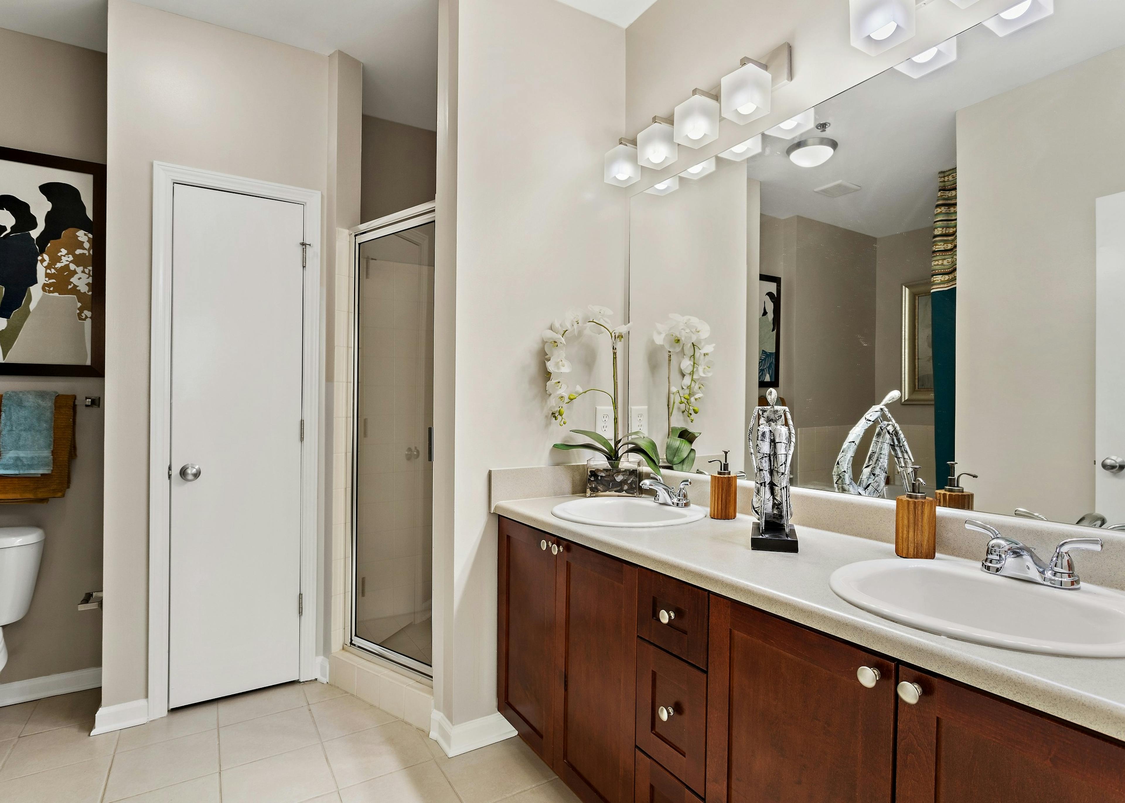 Bathroom with dark wood vanity with two sinks and large mirror above and walk in shower at AMLI Lindbergh apartments