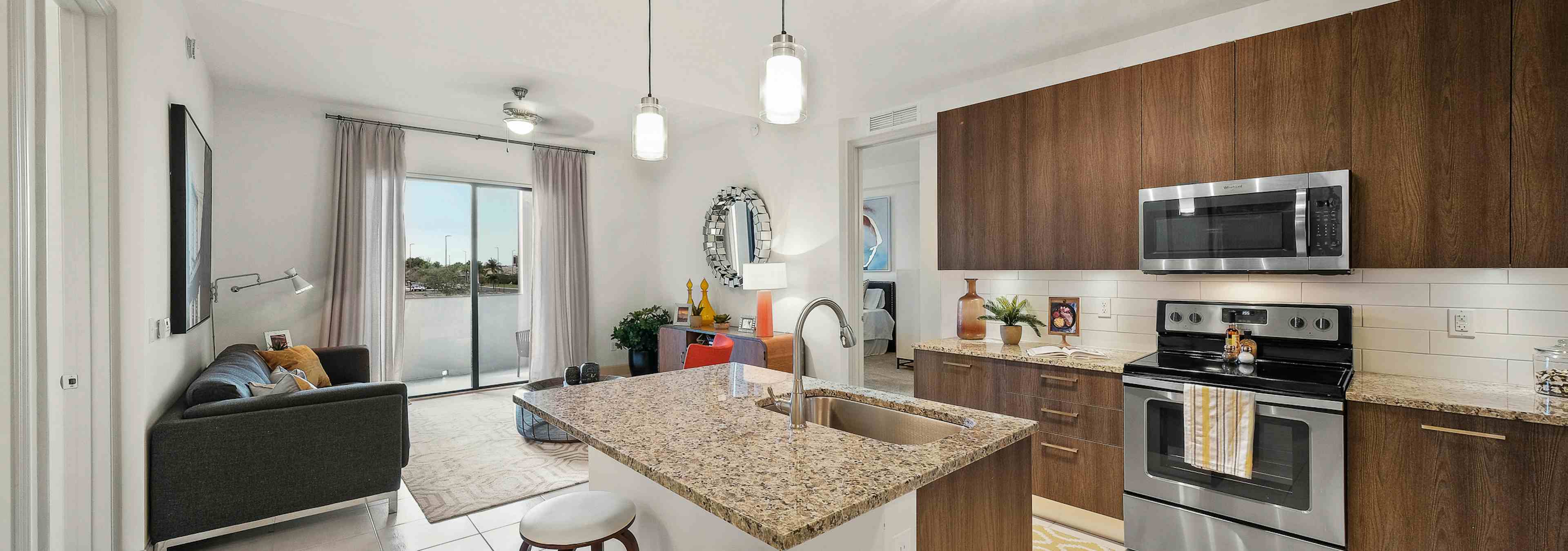 AMLI 8800 apartment with island kitchen with stools, stainless steel appliances, wood cabinetry and peek into living area 