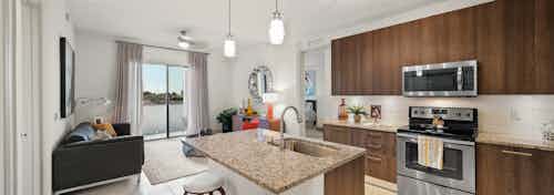 AMLI 8800 apartment with island kitchen with stools, stainless steel appliances, wood cabinetry and peek into living area