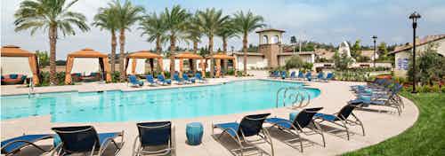 Daytime view of AMLI Spanish Hills apartment swimming pool area with plentiful lounge seating and cabanas and palm trees