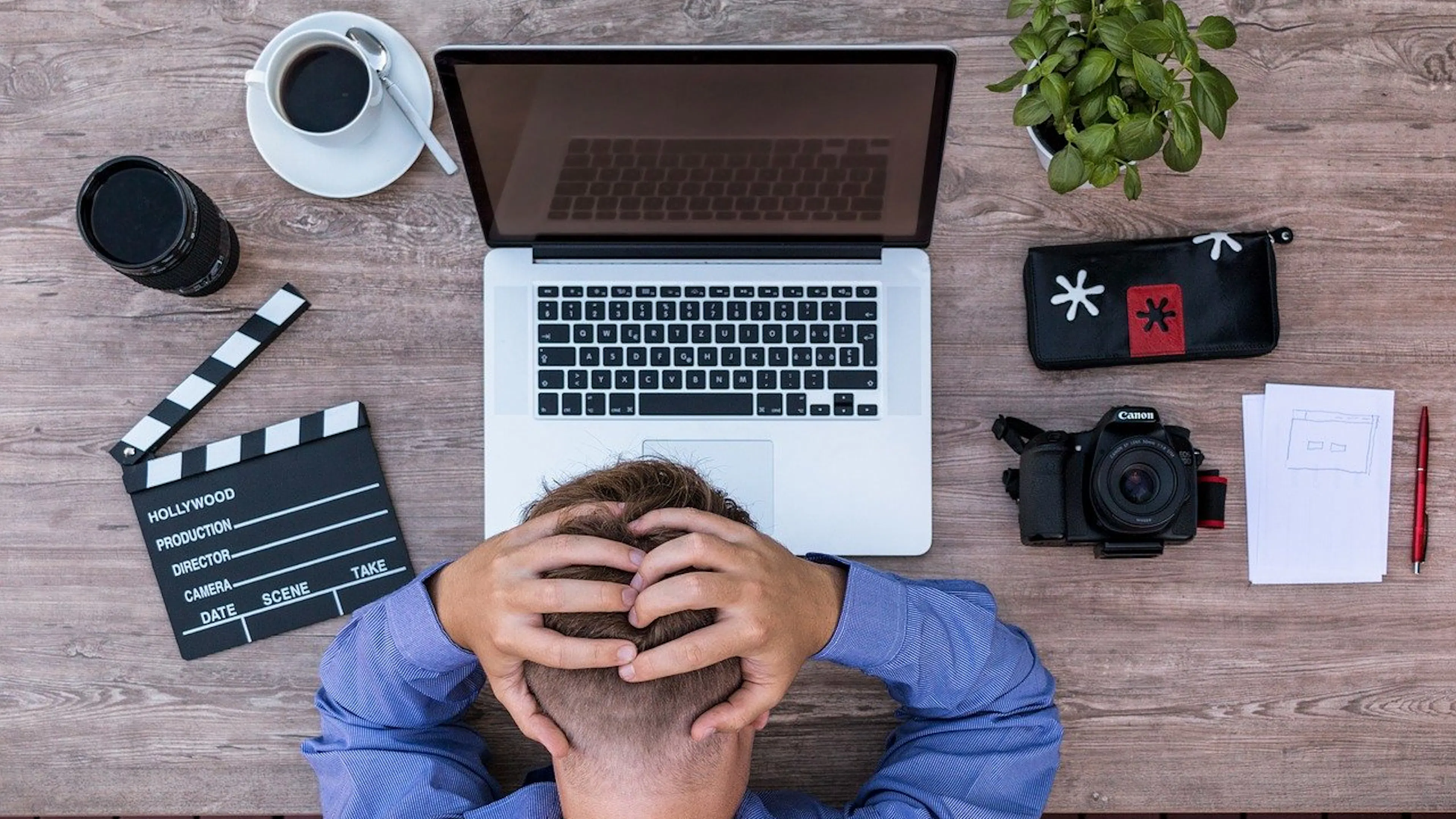 A man with his head held in his hands in front of a laptop and camera equipment
