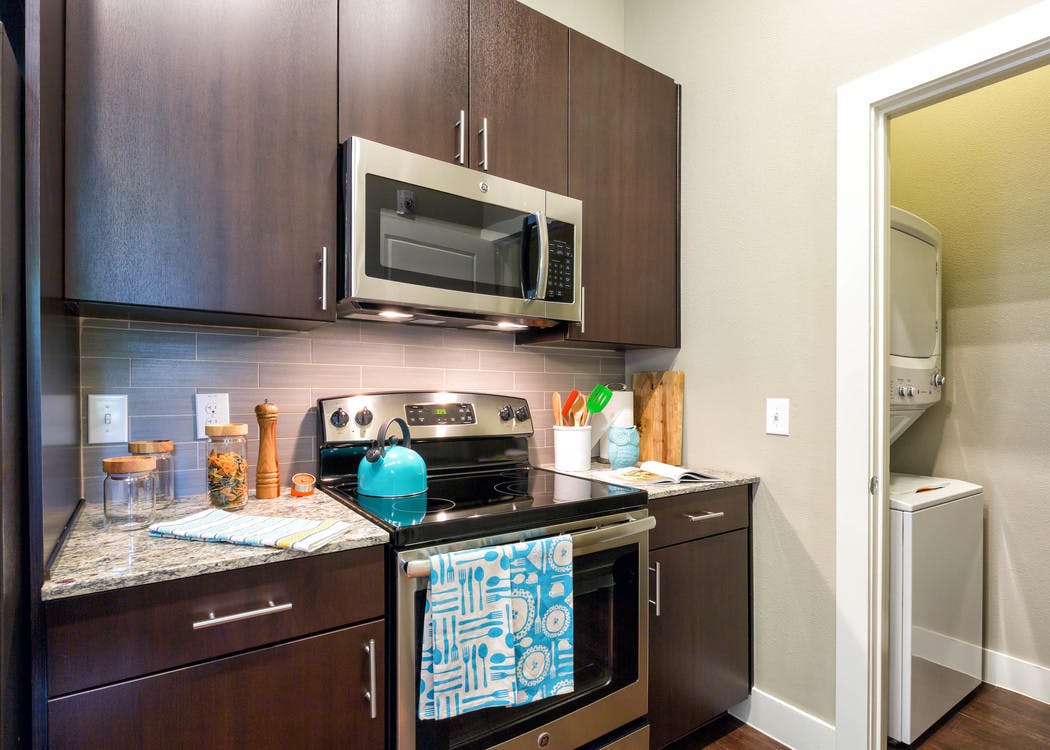 Close up of AMLI at Mueller dark kitchen cabinetry with beige backsplash and granite countertops with peek into laundry area