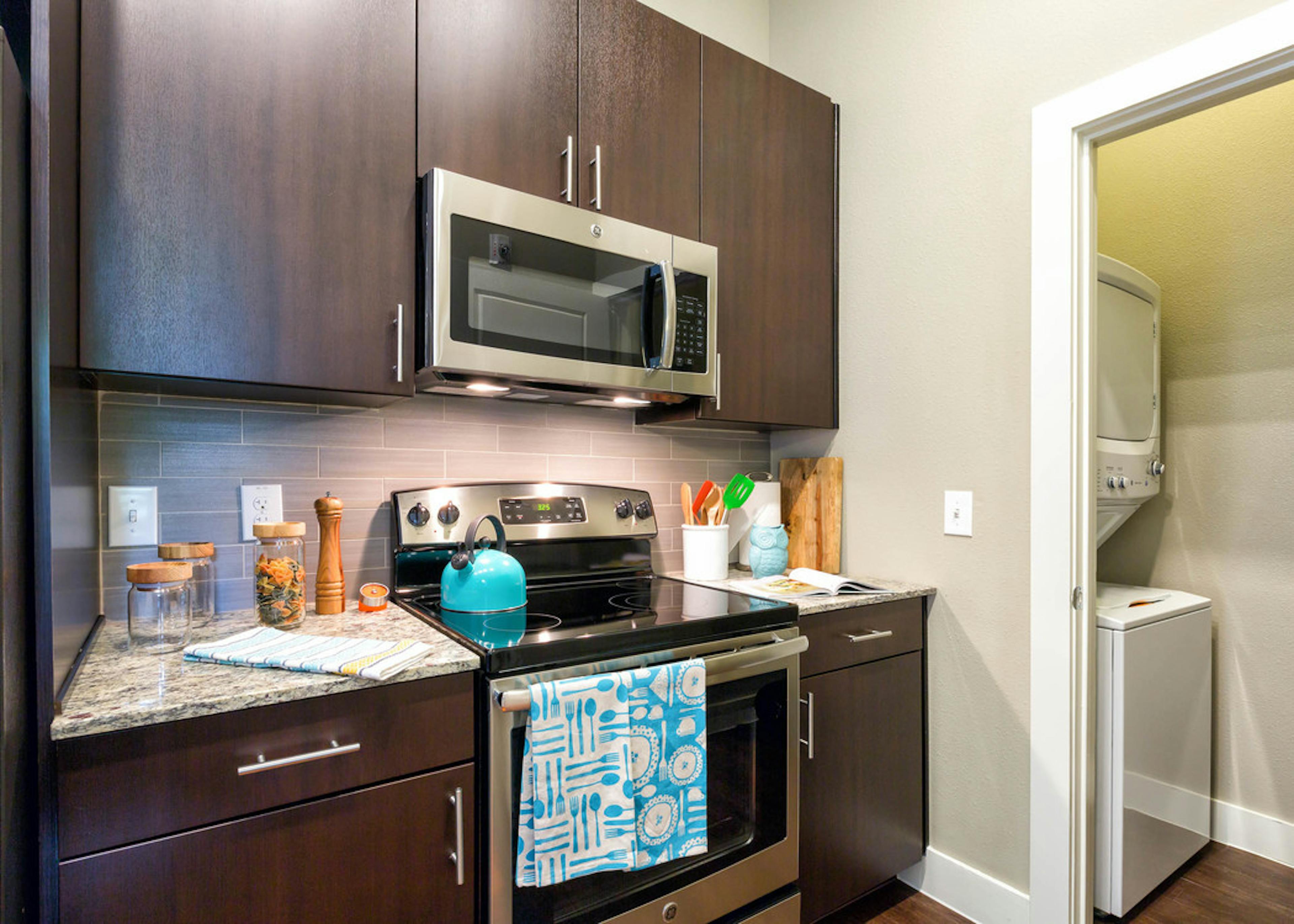 Close up of AMLI at Mueller dark kitchen cabinetry with beige backsplash and granite countertops with peek into laundry area
