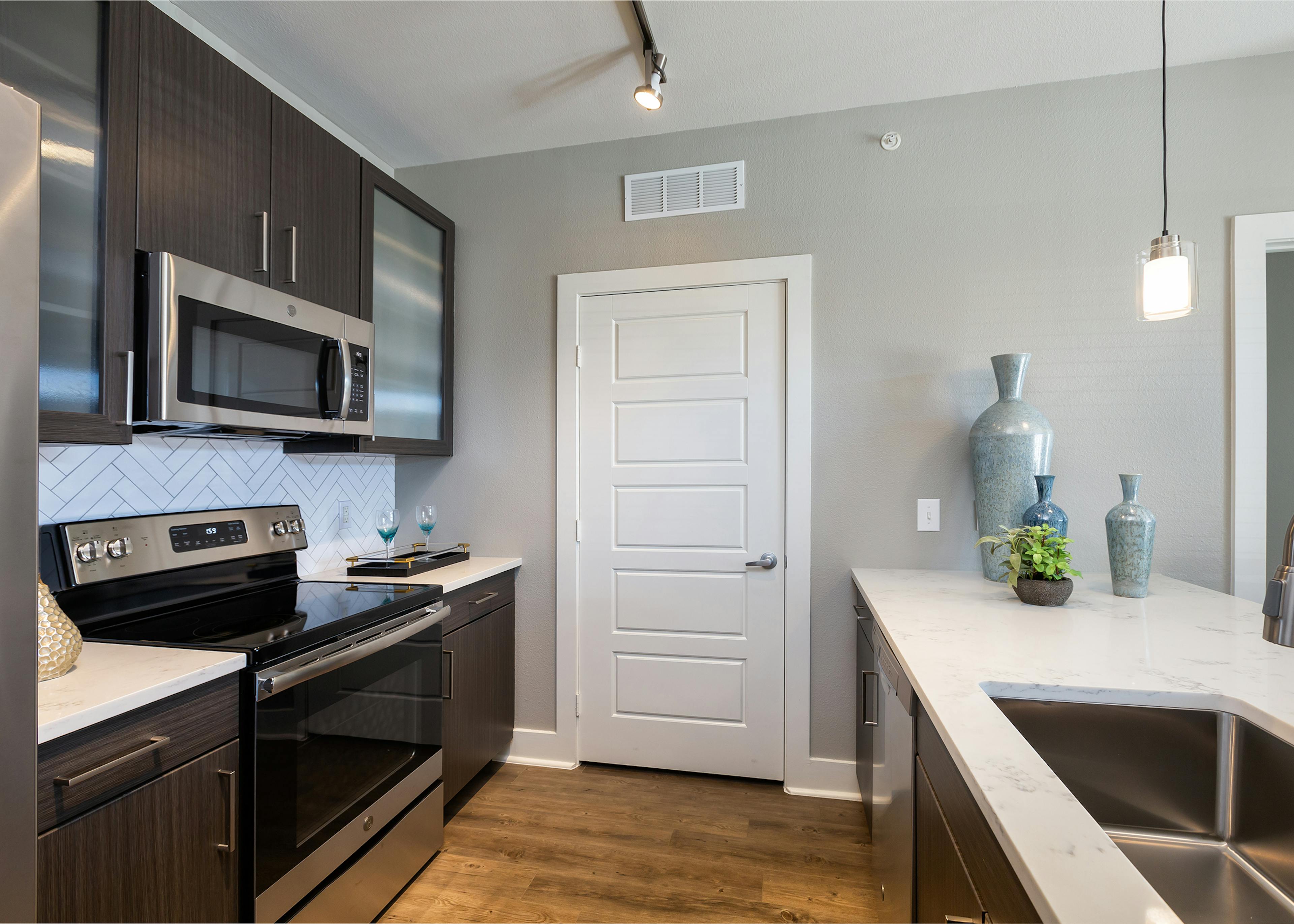 AMLI South Shore apartment kitchen with stainless steel appliances and quartz countertops with light ceramic tile backsplash and white door