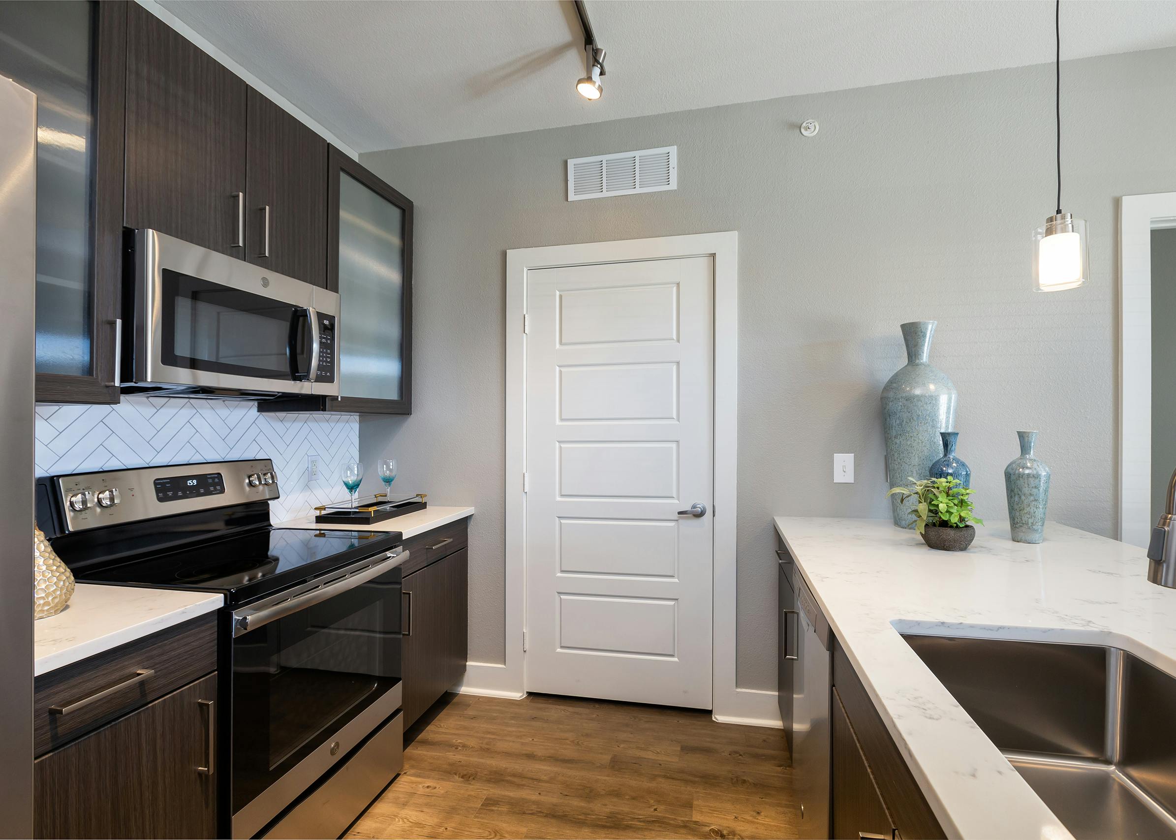 AMLI South Shore apartment kitchen with stainless steel appliances and quartz countertops with light ceramic tile backsplash and white door