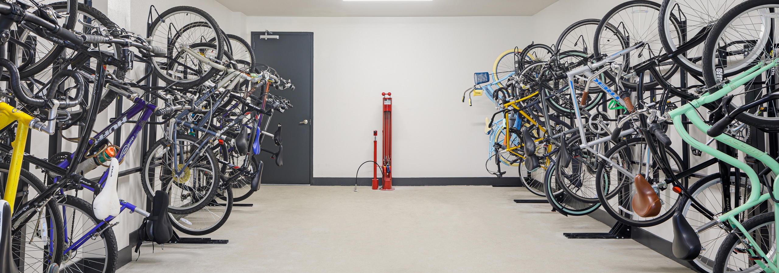 Bicycle storage room at AMLI Addison apartments with red tire pump and full black bicycle racks against two white walls