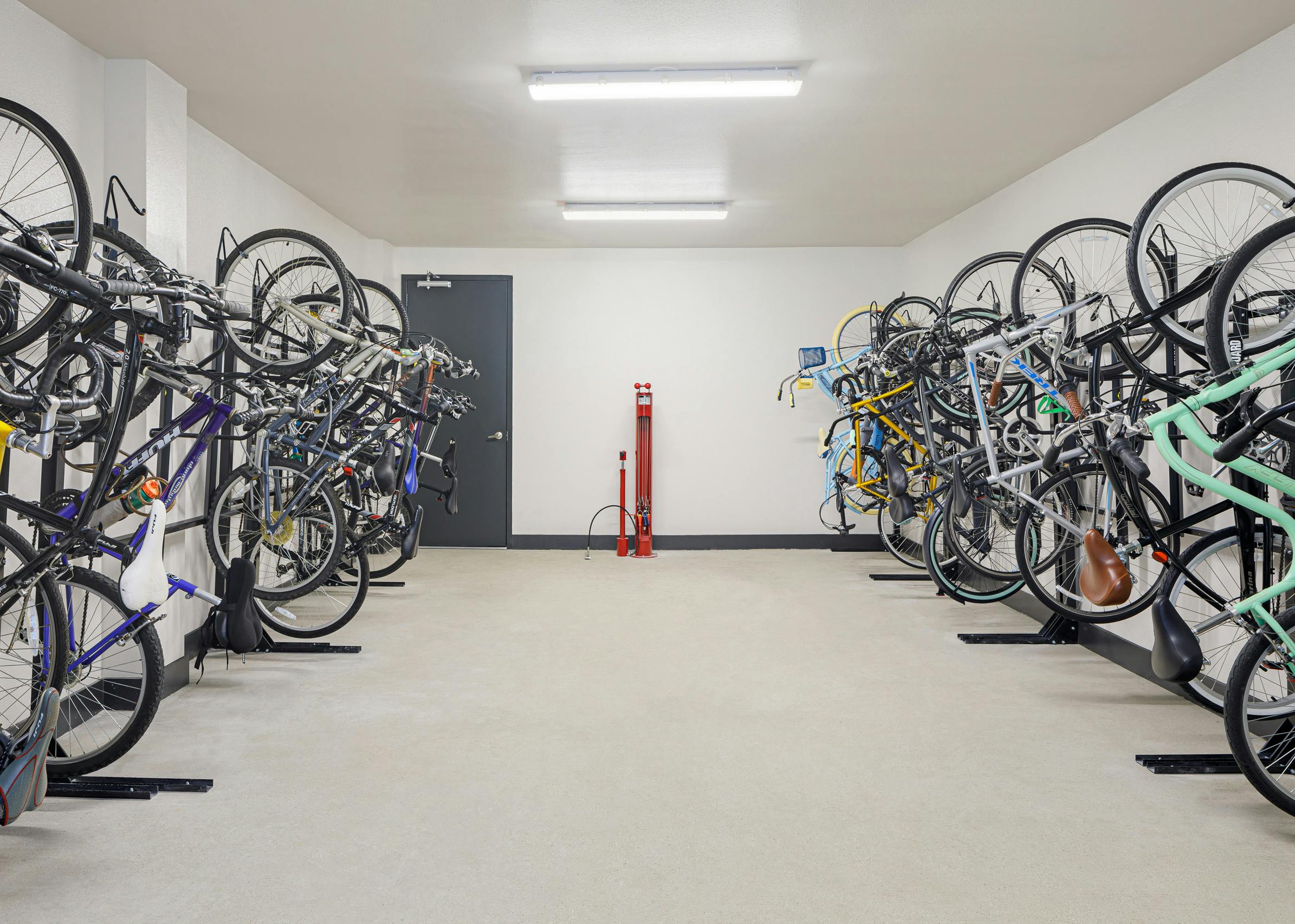 Bicycle storage room at AMLI Addison apartments with red tire pump and full black bicycle racks against two white walls