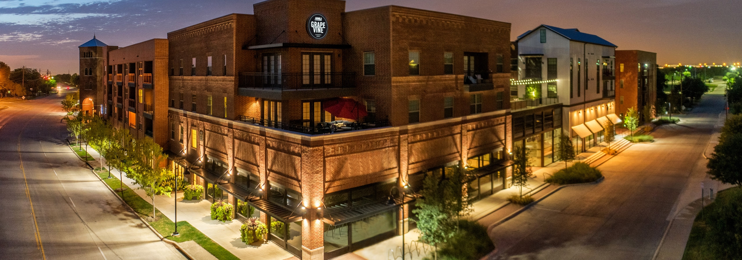 Night view of AMLI Grapevine apartment building brick facade with illuminated circular sign and tree lined streets