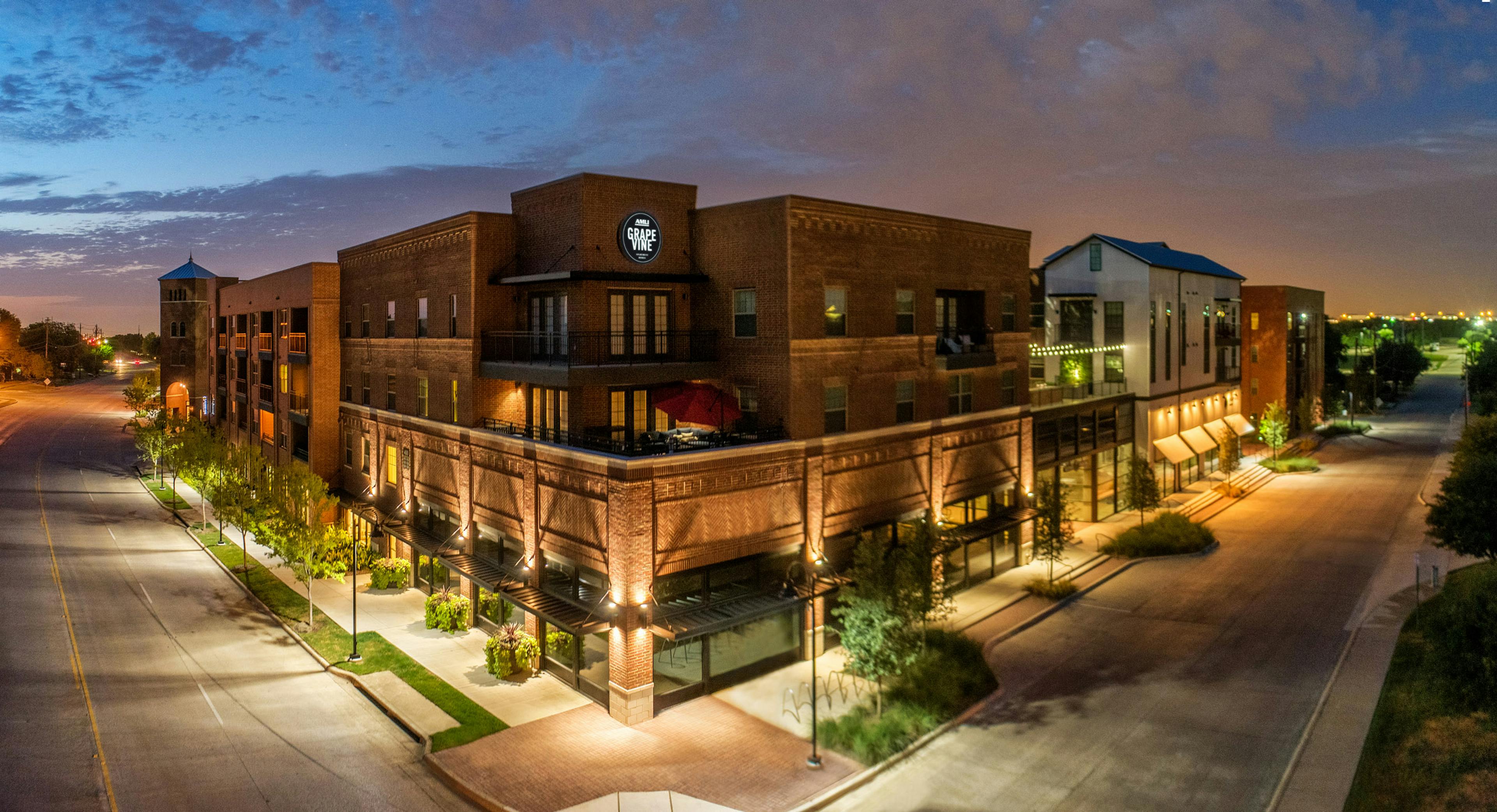 Night view of AMLI Grapevine apartment building brick facade with illuminated circular sign and tree lined streets