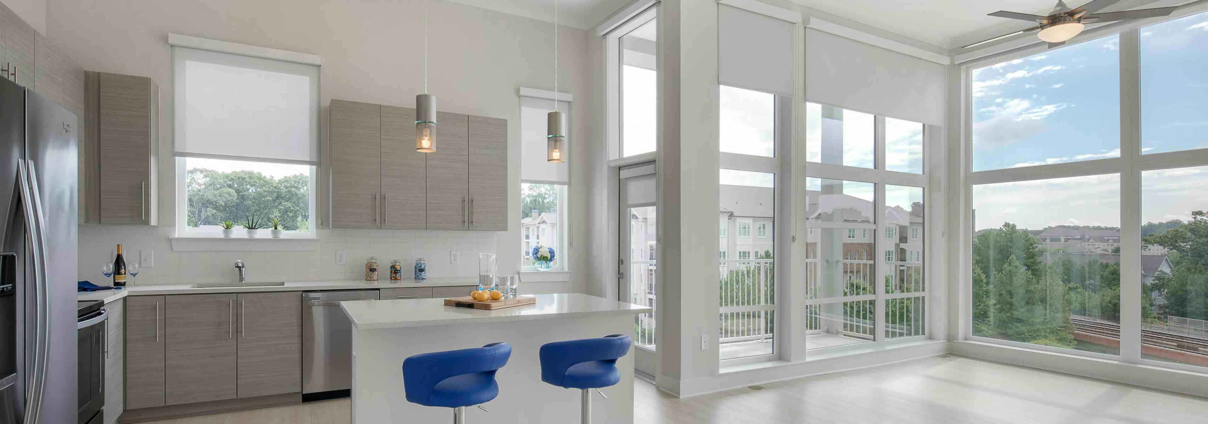 AMLI Buckhead kitchen with grey wood cabinets and an island with blue barstools and floor to ceiling windows with nature view