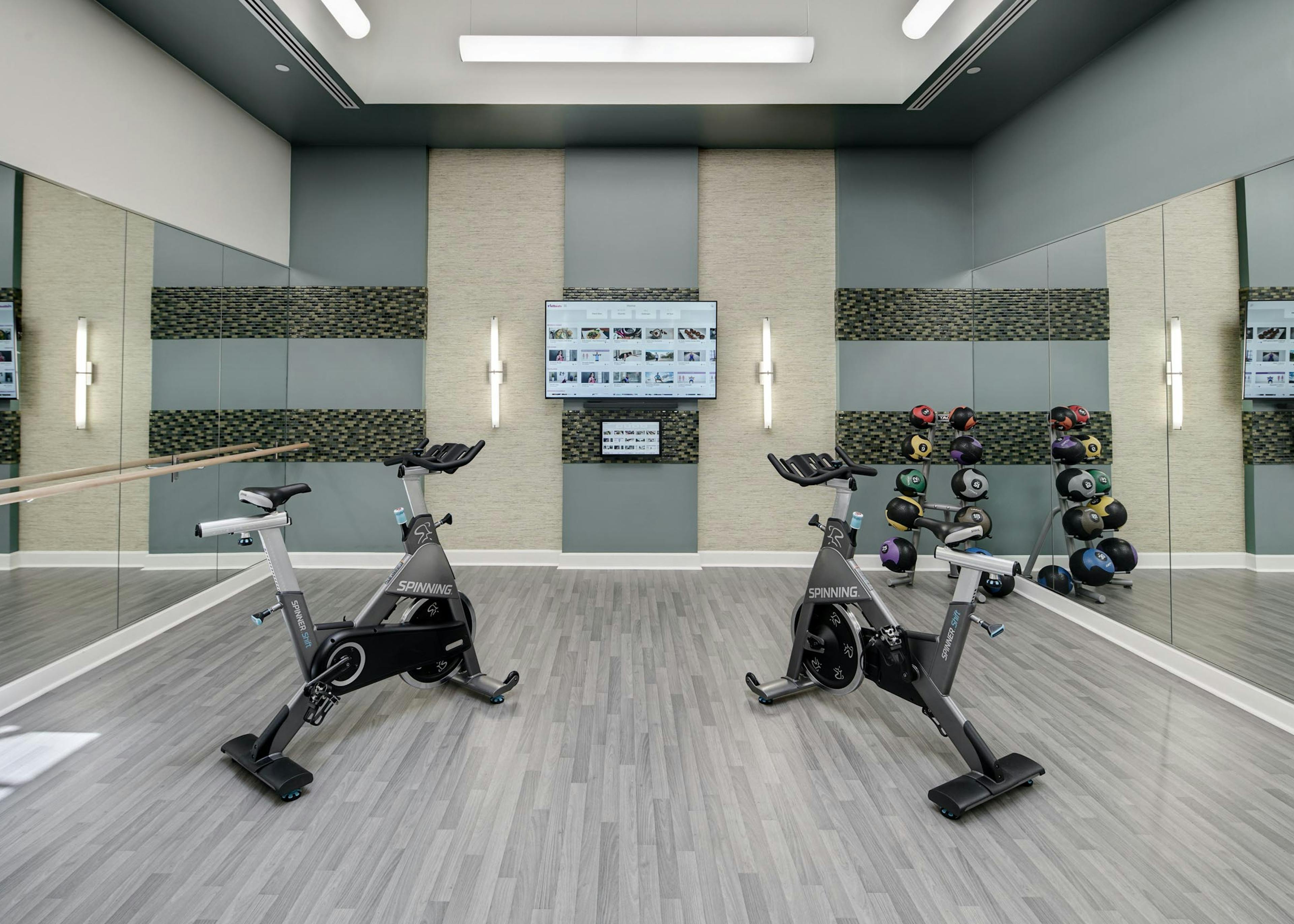 Close up of two exercise machines in an AMLI Evanston amenity space surrounded by mirrored walls with a flat screen TV