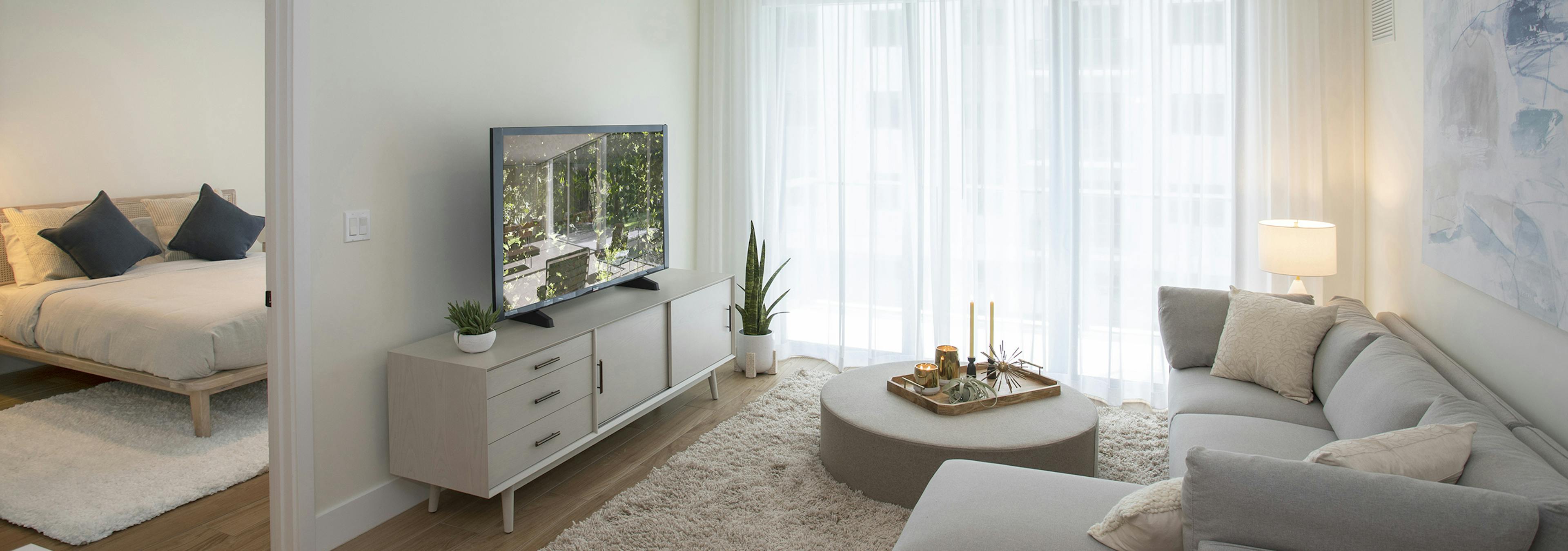 AMLI Midtown Miami apartment living room with sofa and round coffee table and TV sitting on chest and peek into bedroom