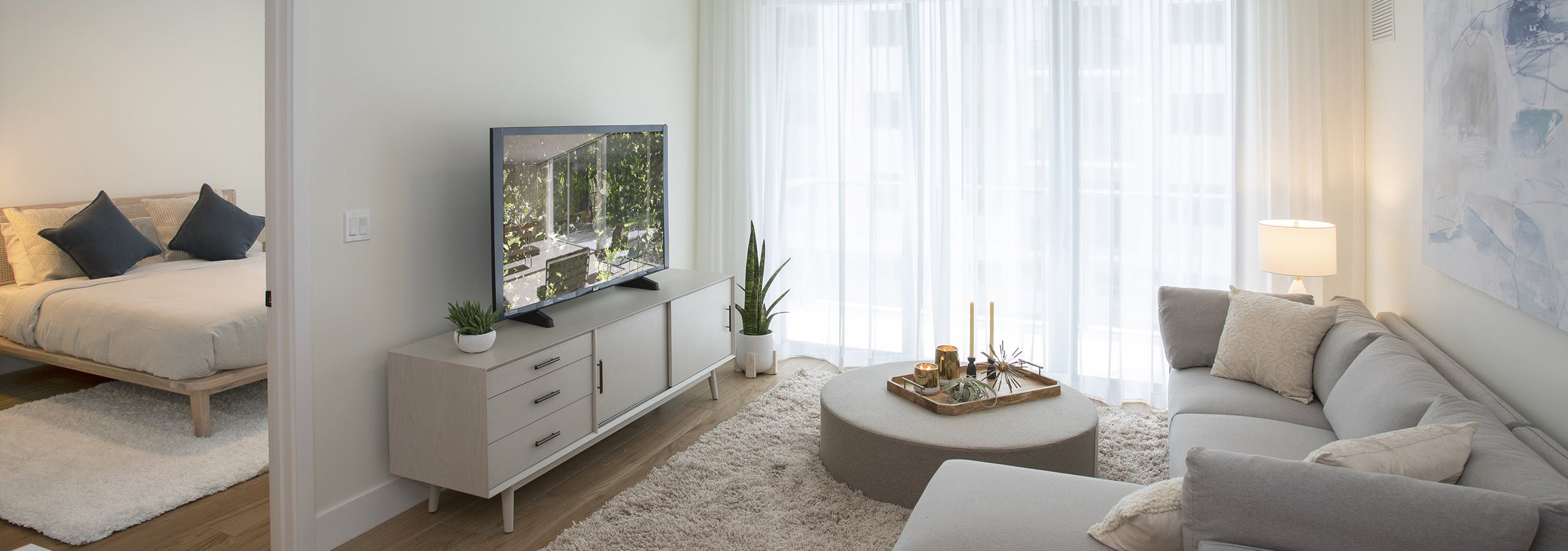 AMLI Midtown Miami apartment living room with sofa and round coffee table and TV sitting on chest and peek into bedroom