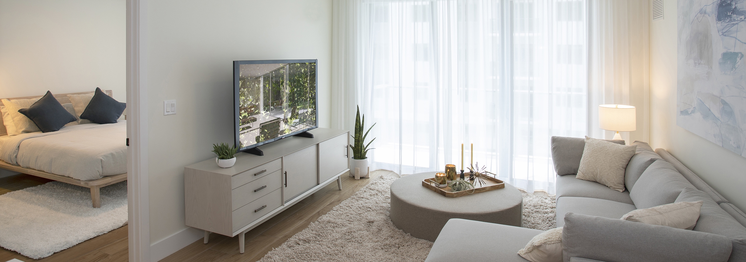 AMLI Midtown Miami apartment living room with sofa and round coffee table and TV sitting on chest and peek into bedroom