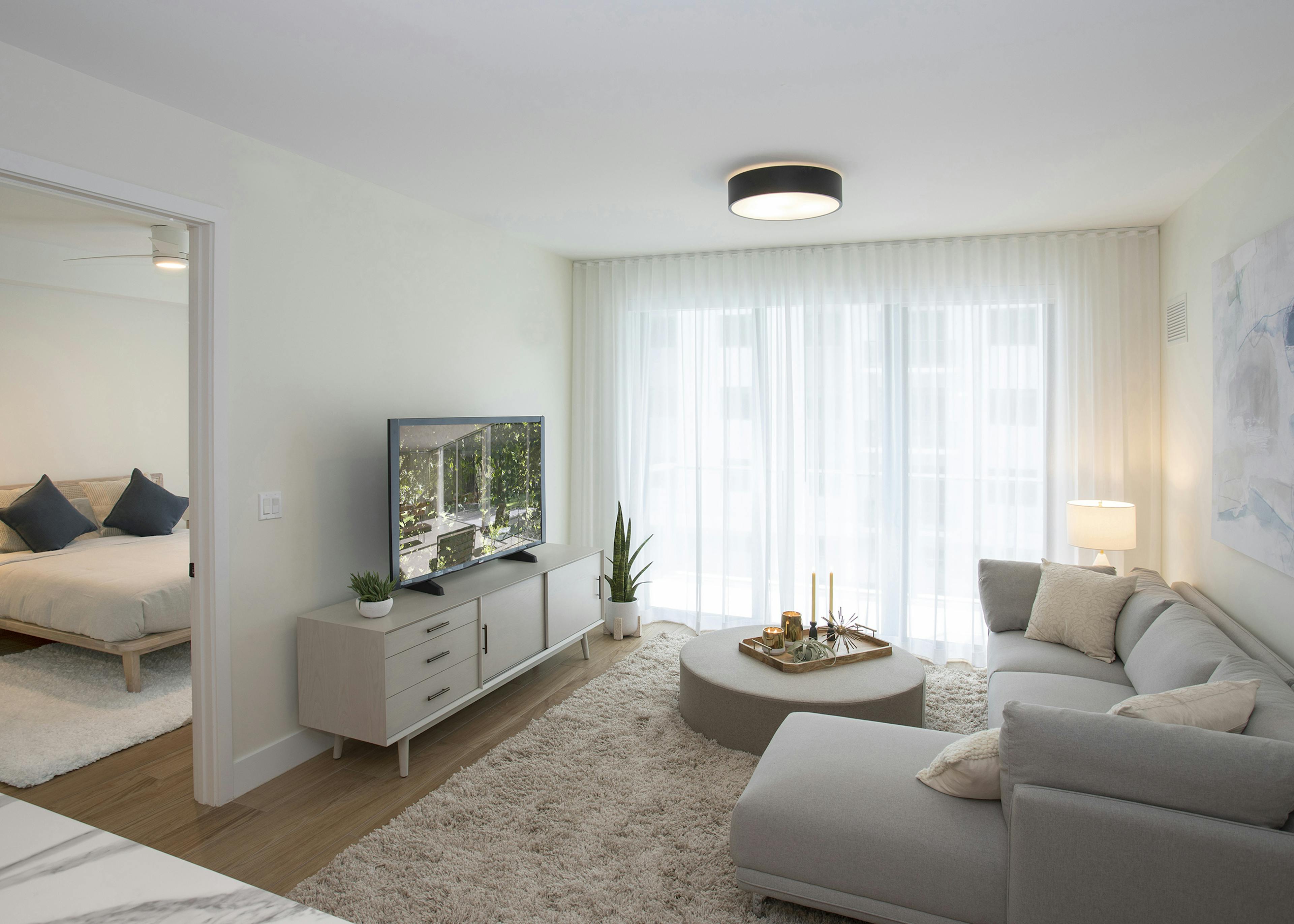 AMLI Midtown Miami apartment living room with sofa and round coffee table and TV sitting on chest and peek into bedroom