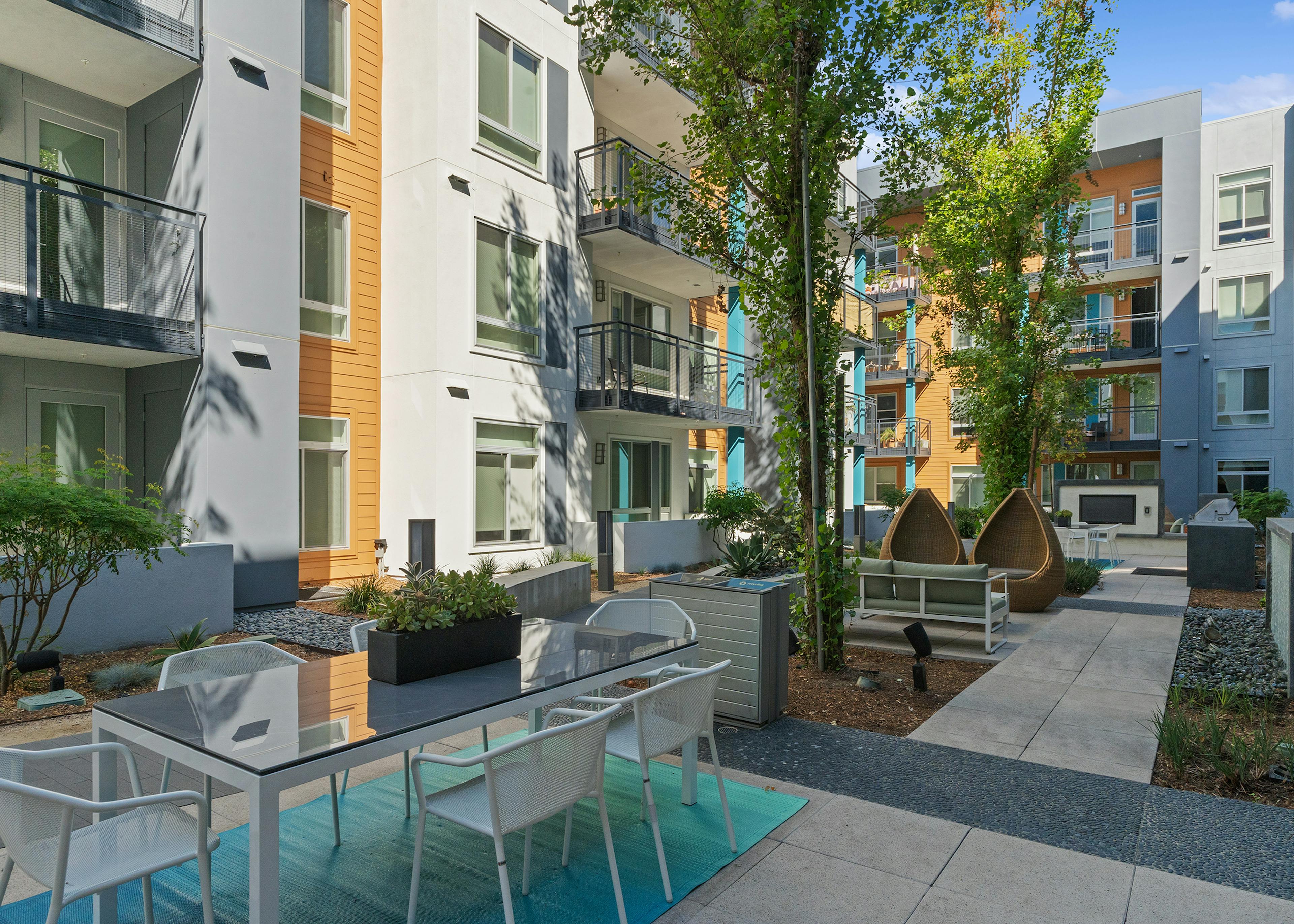 A sunny landscaped courtyard with tables and other seating options and a big screen TV at AMLI Uptown Orange apartments