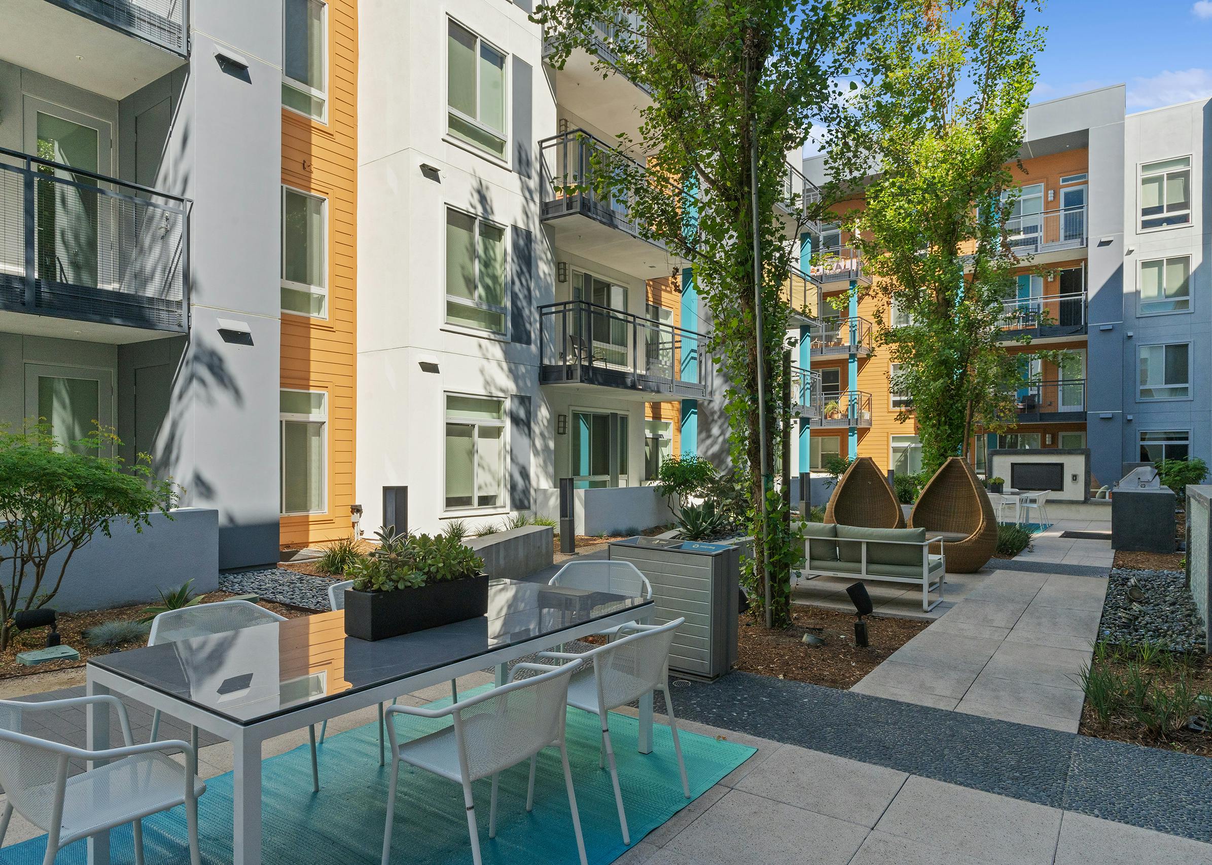 A sunny landscaped courtyard with tables and other seating options and a big screen TV at AMLI Uptown Orange apartments