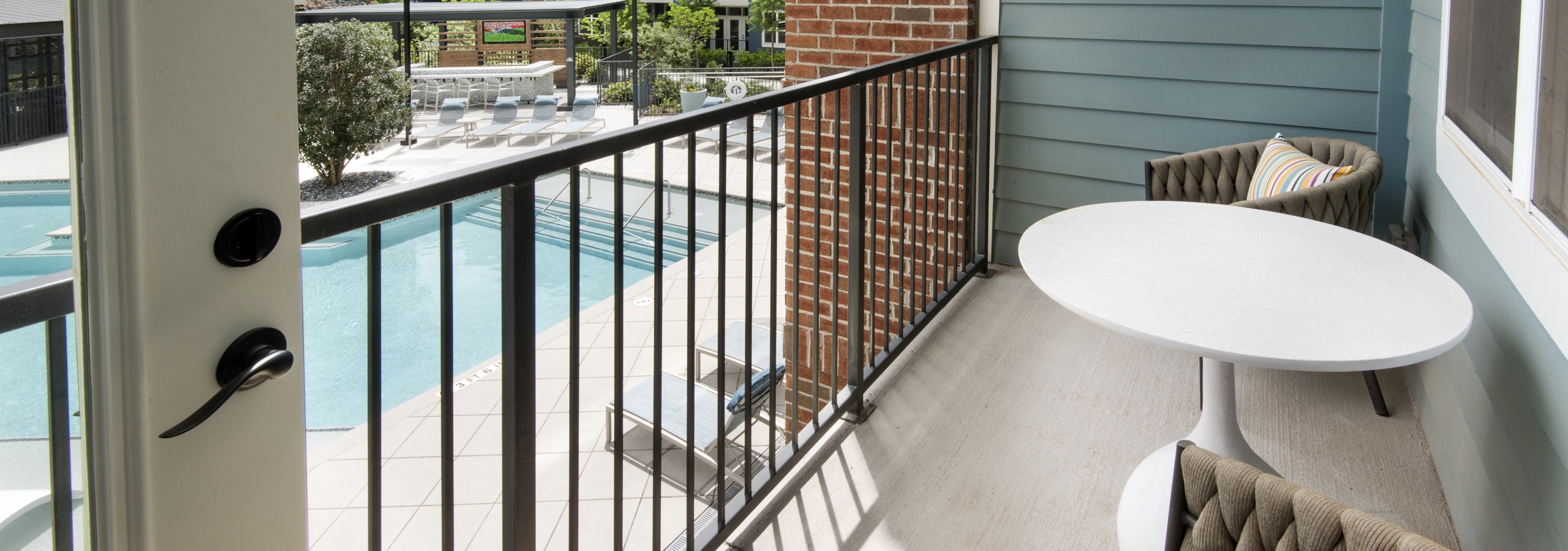 Exterior view of a balcony on one of the AMLI Decatur apartments with two chairs and a table overlooking the pool area