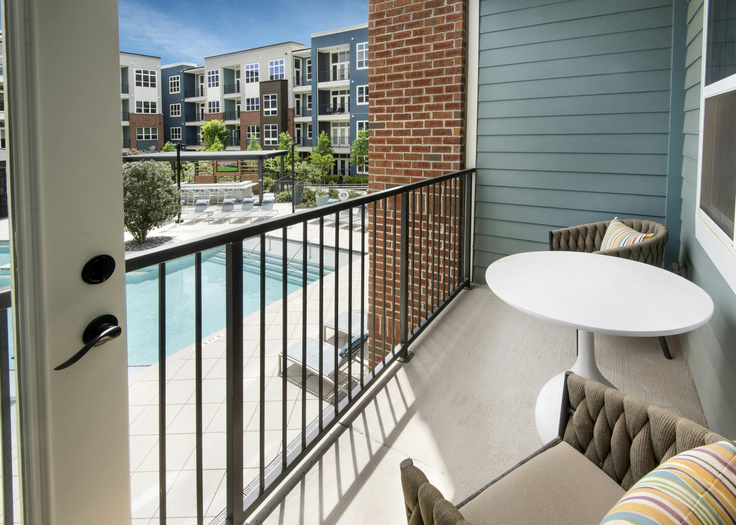 Exterior view of a balcony on one of the AMLI Decatur apartments with two chairs and a table overlooking the pool area