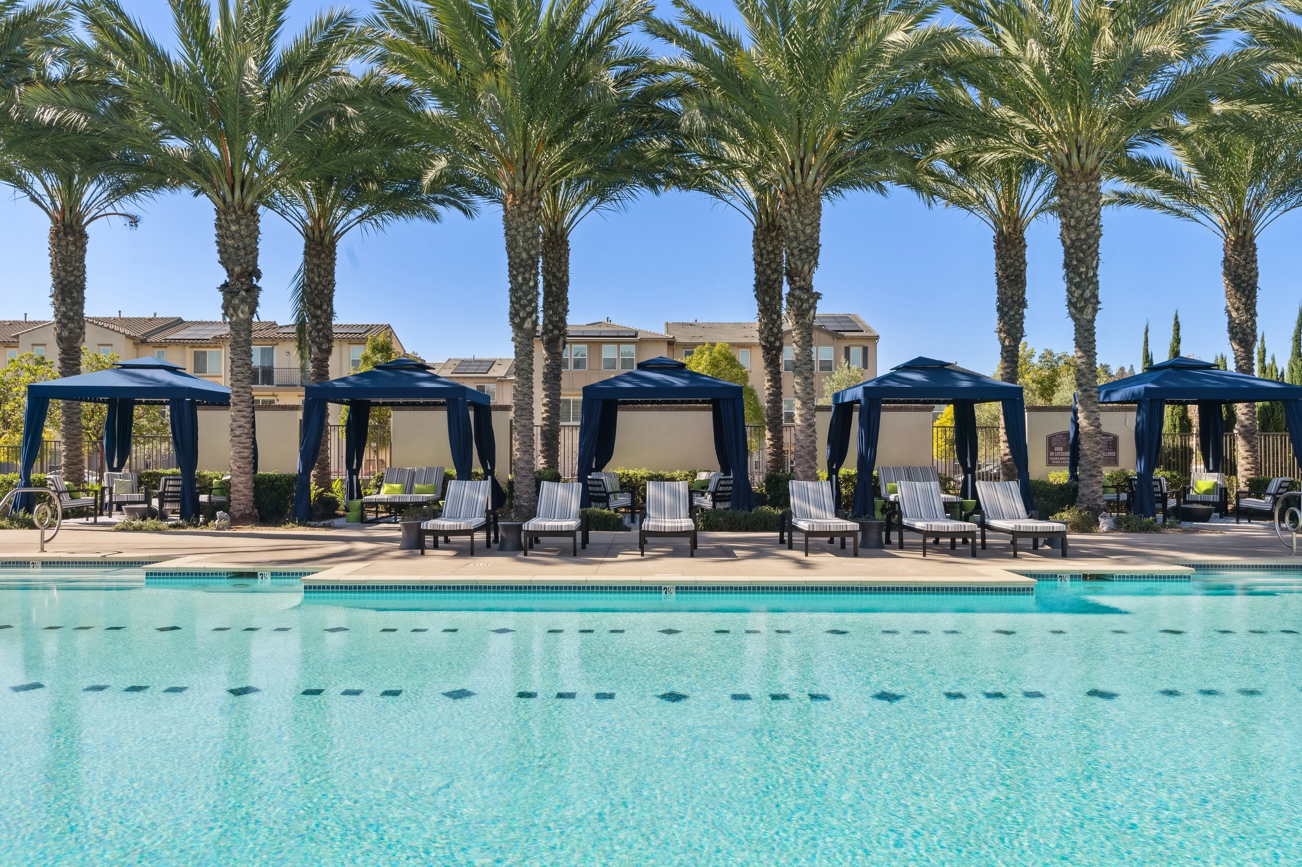 AMLI Spanish Hills swimming sparkling pool showcasing palm trees hovering over blue cabanas and striped lounge seating 