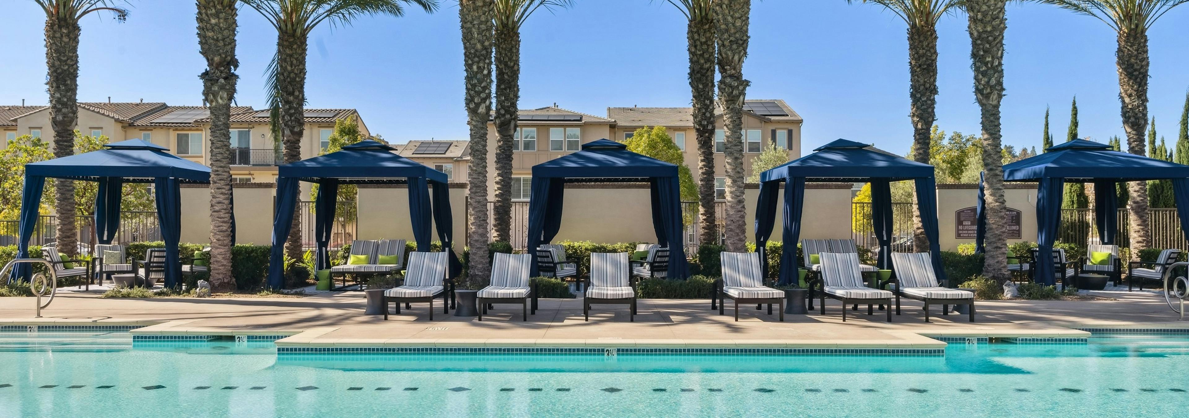 AMLI Spanish Hills swimming sparkling pool showcasing palm trees hovering over blue cabanas and striped lounge seating 