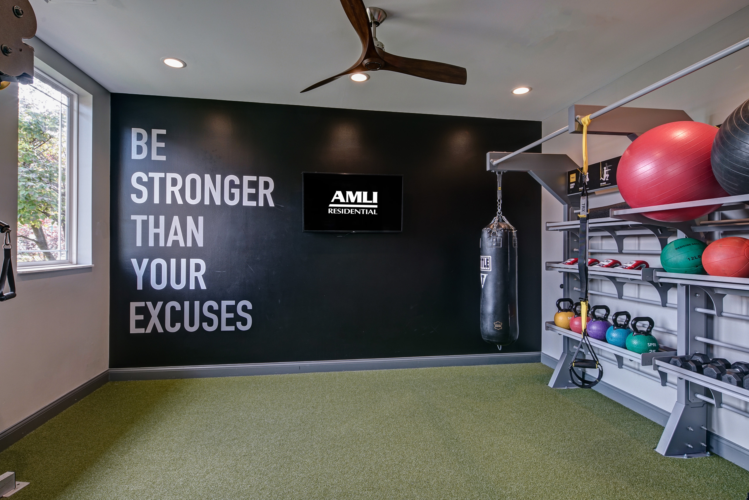 Fitness center at AMLI at Seven Bridges with punching bag and shelves of kettlebells and weights and balls and black back wall