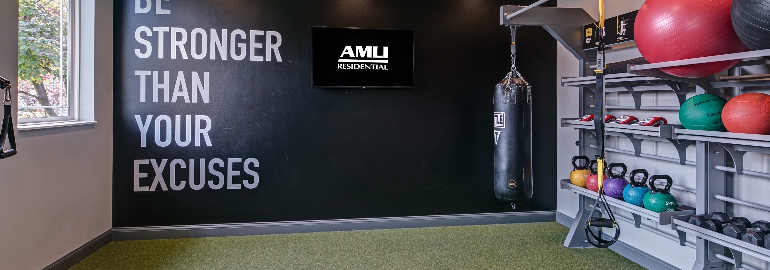 Fitness center at AMLI at Seven Bridges with punching bag and shelves of kettlebells and weights and balls and black back wall