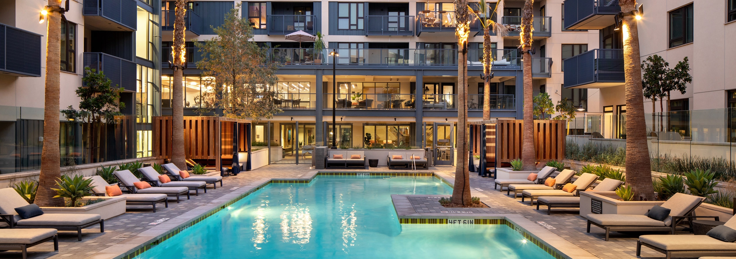 Dusk view of AMLI Old Pasadena apartment swimming pool surrounded by palm trees and plentiful lounge seating with pillows