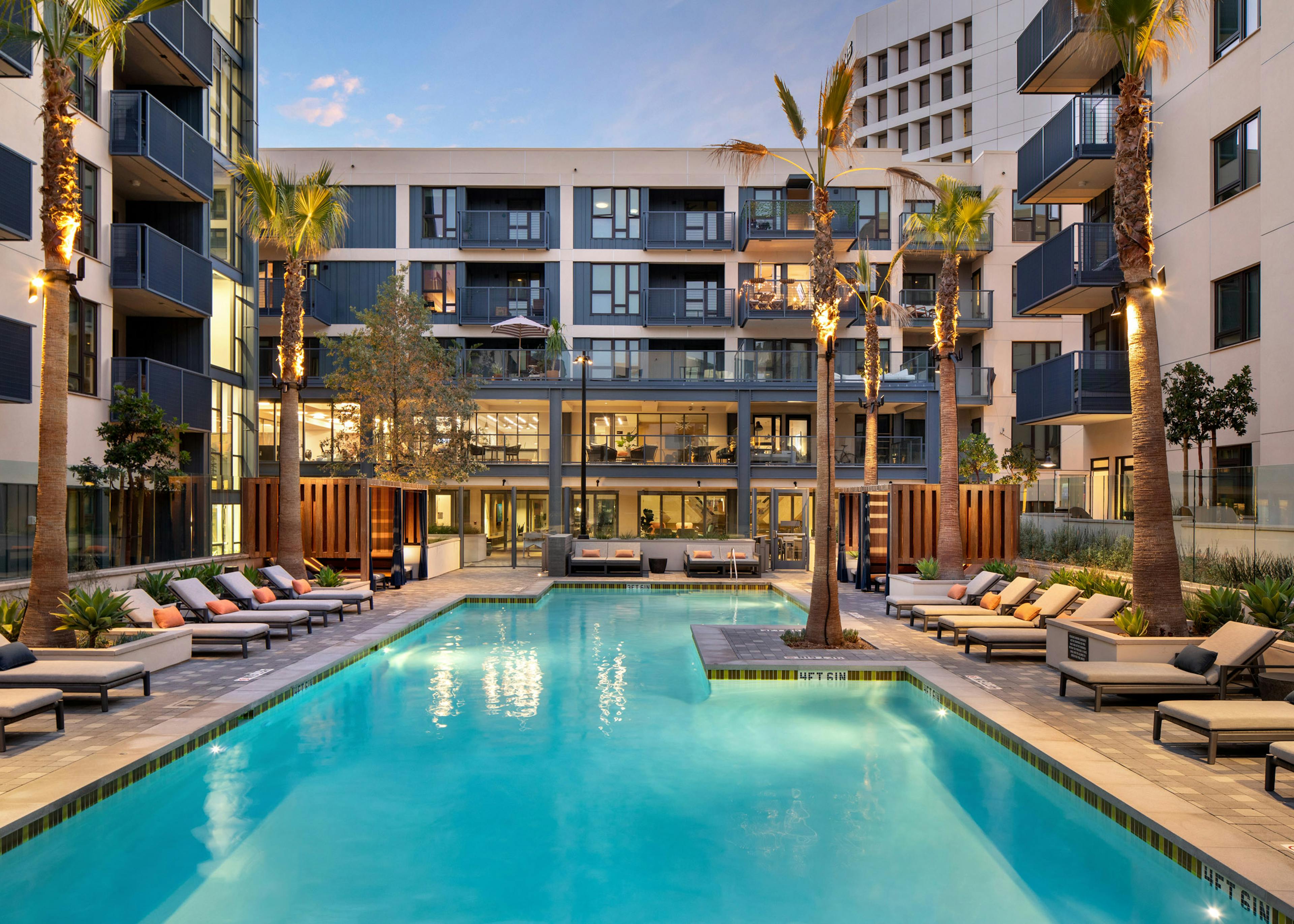 Dusk view of AMLI Old Pasadena apartment swimming pool surrounded by palm trees and plentiful lounge seating with pillows