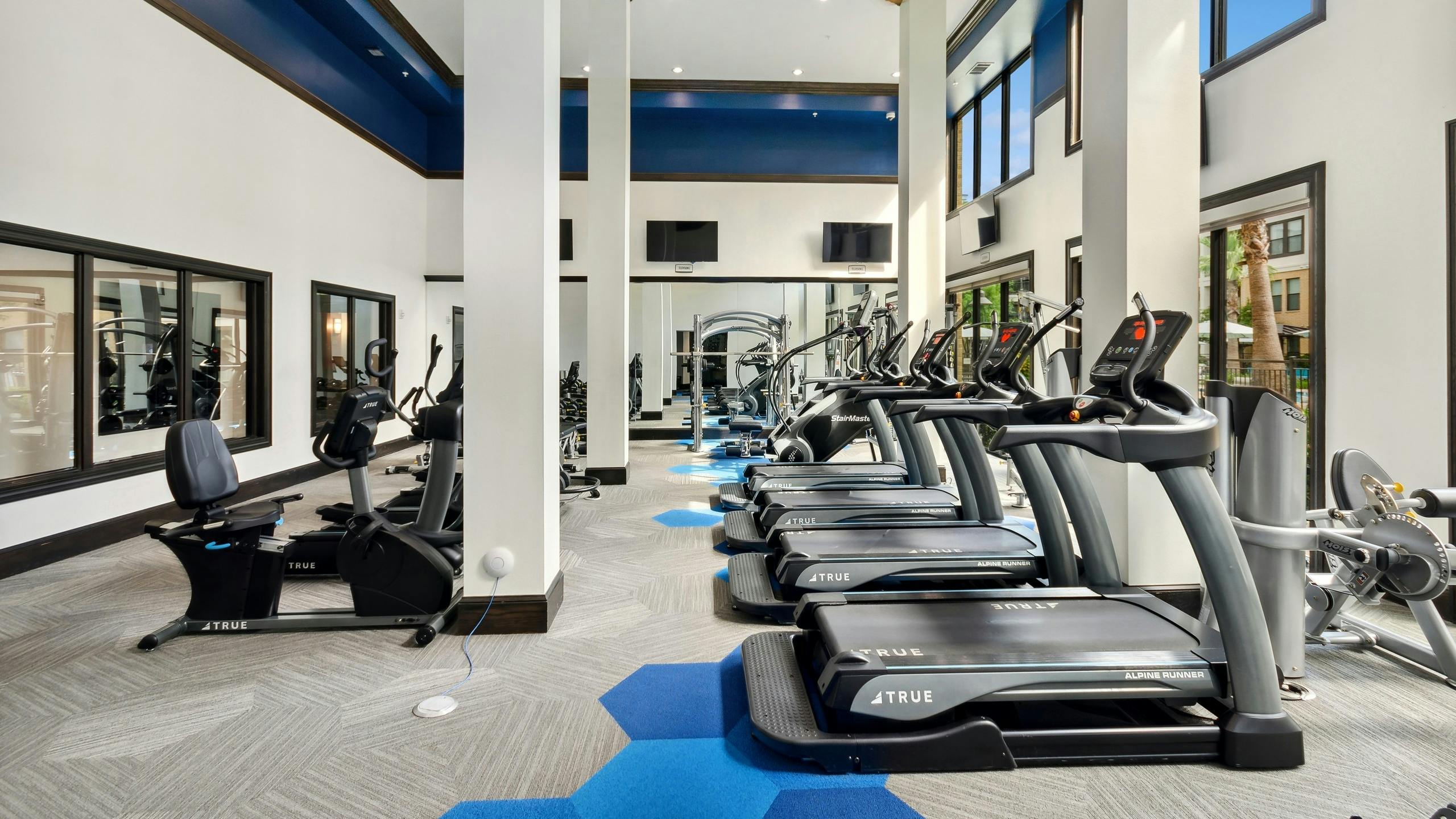 AMLI Campion Trail fitness center with treadmills and cardio machines and mounted TVs and large two-story windows