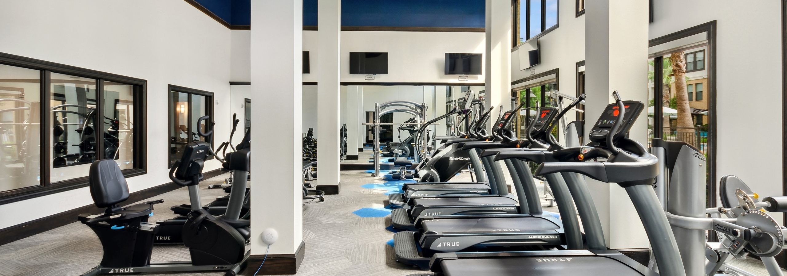 AMLI Campion Trail fitness center with treadmills and cardio machines and mounted TVs and large two-story windows