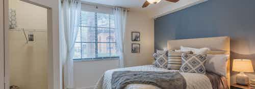 AMLI Toscana Place apartment bedroom with white and gray bedding and blue wall and open closet and window with blinds