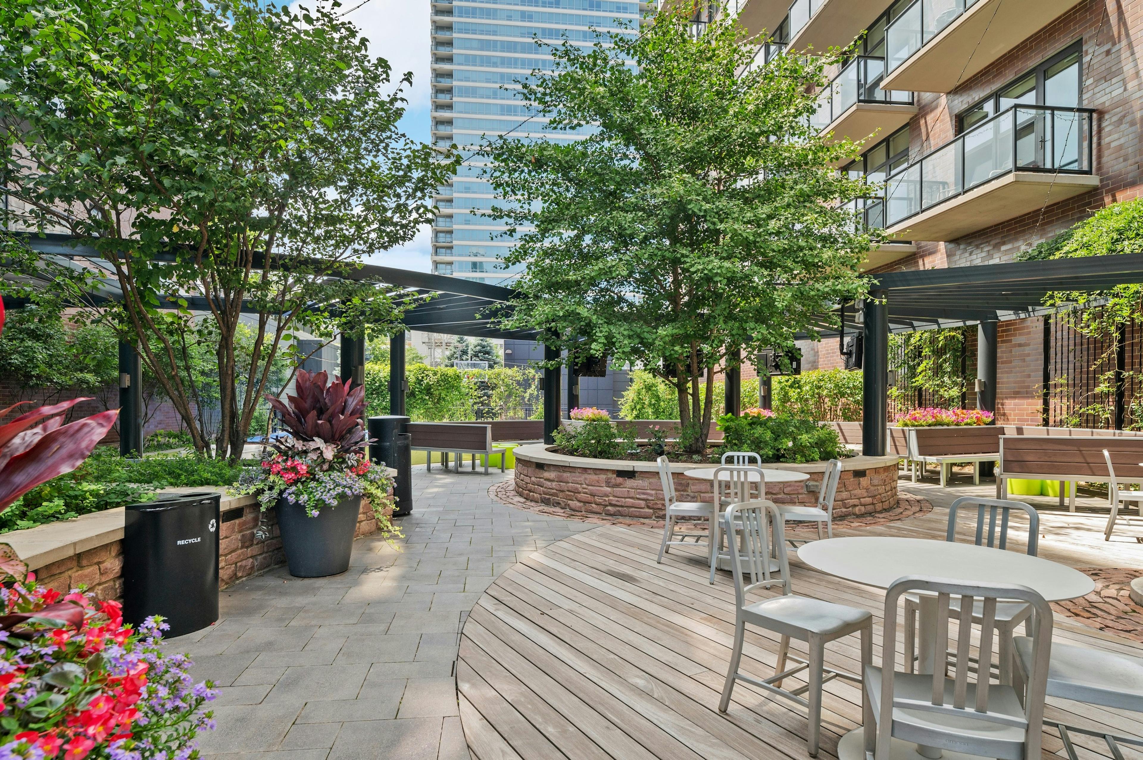 Daytime view of AMLI Lofts courtyard lounge with gray dining tables and wood bench seating surrounded by lush greenery