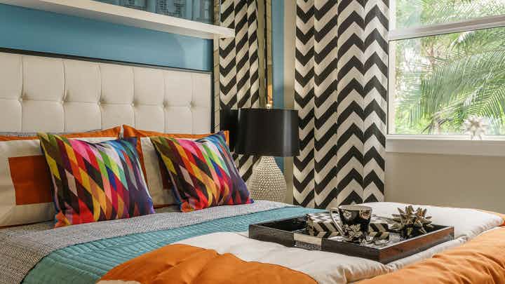 Interior view of an AMLI Sawgrass Village apartment bedroom with a bed underneath a shelf, colorful bedding and a window view