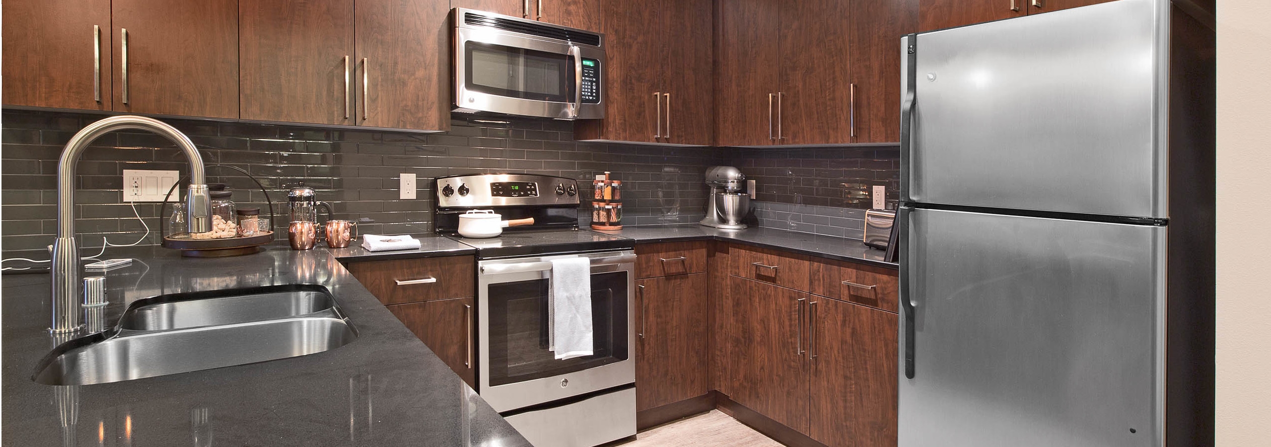 Interior view of AMLI Mark24 apartment kitchen with dark cabinets black back splash black quartz counter tops and stainless steel appliances