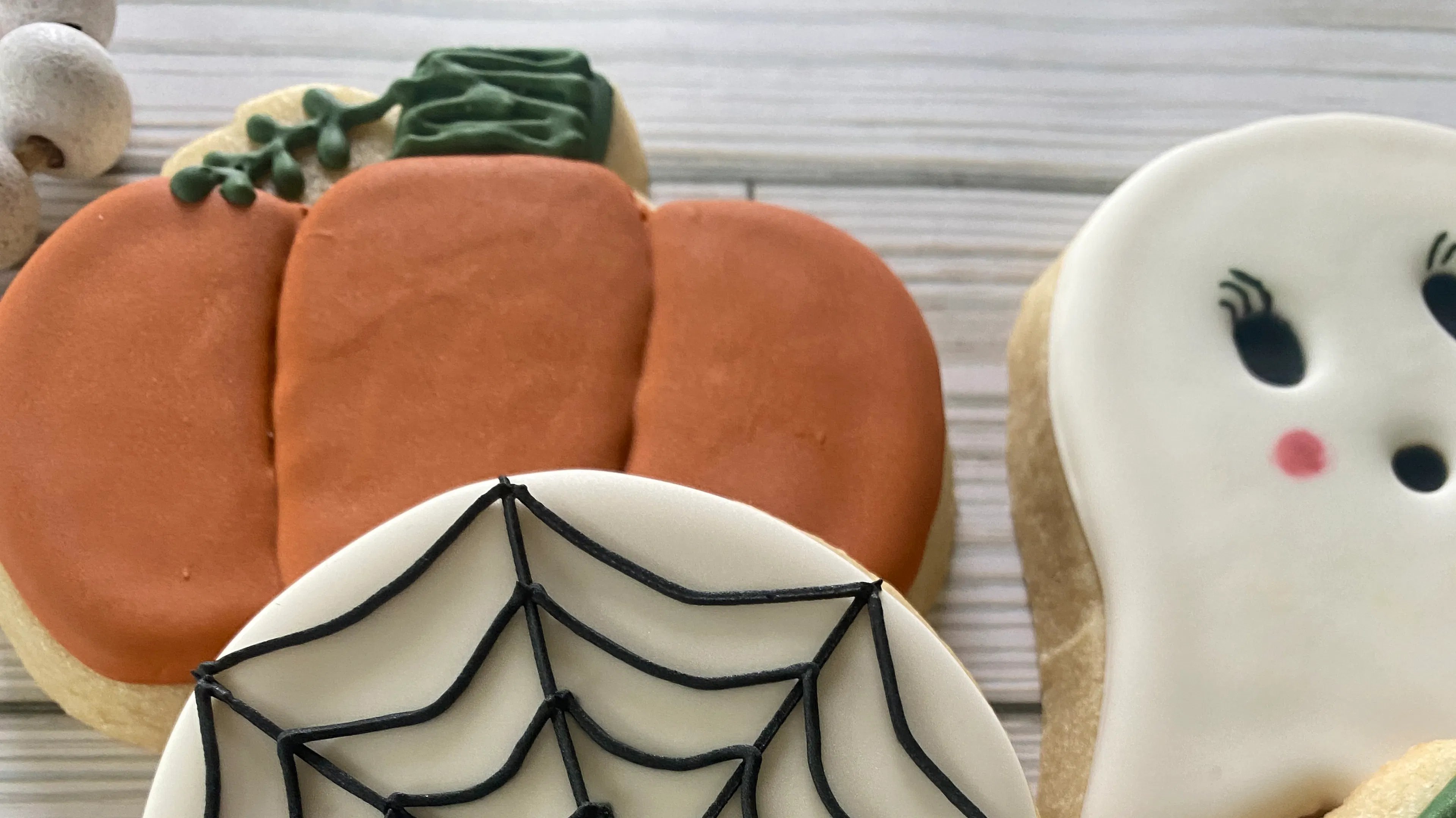 A close up of three Halloween sugar cookies decorated to look like a pumpkin a ghost and a spider web